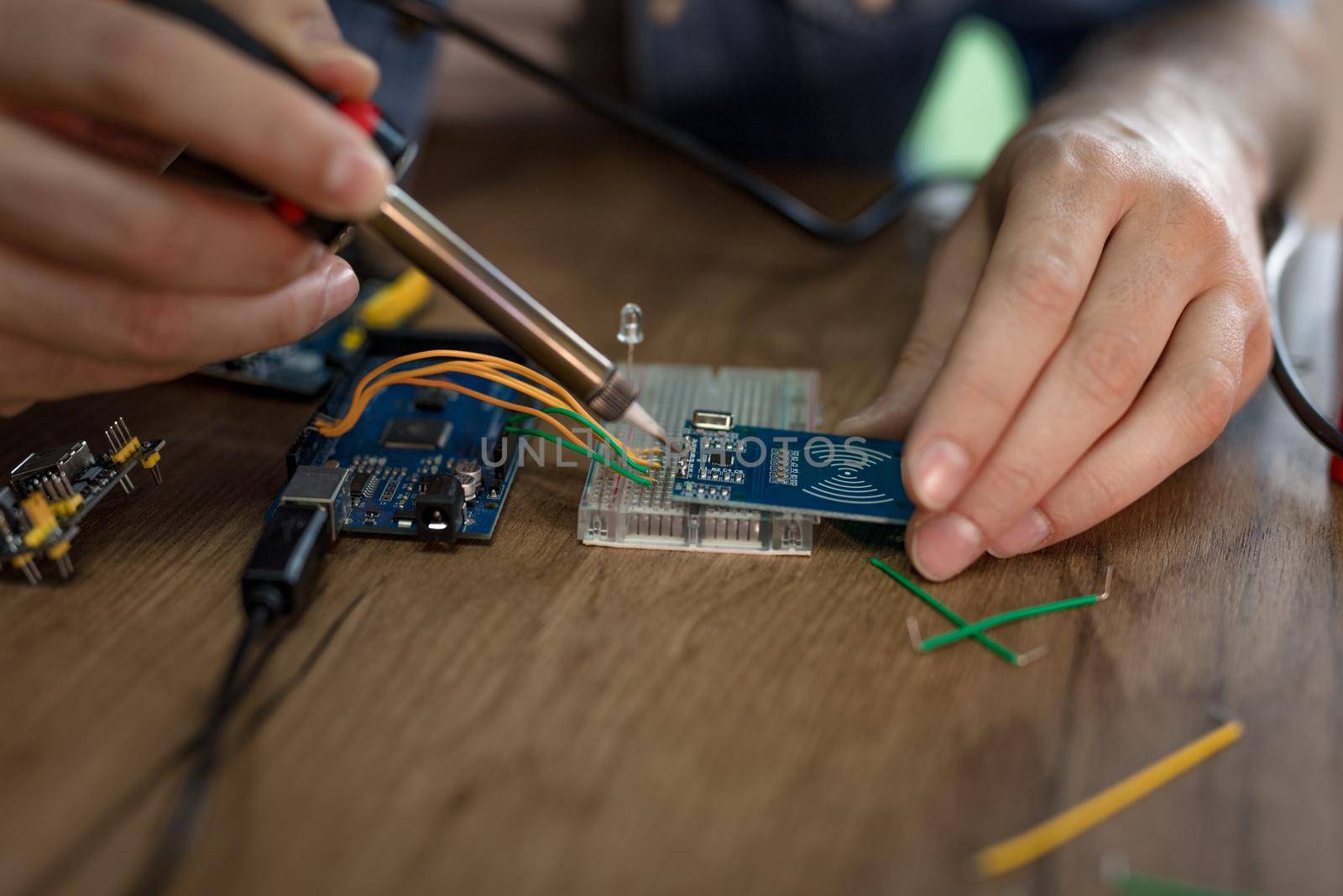 Close-up of a male hands soldering circuit board by soldering iron on the table.