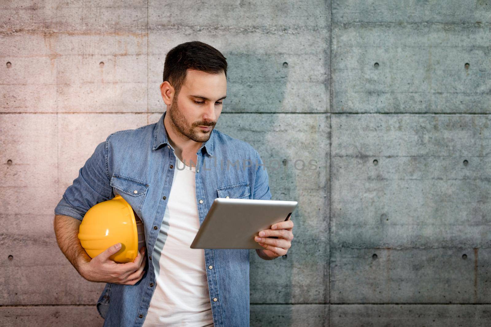Young handsome successful entrepreneur looking on his tablet, checking plans before starting to work on construction site.