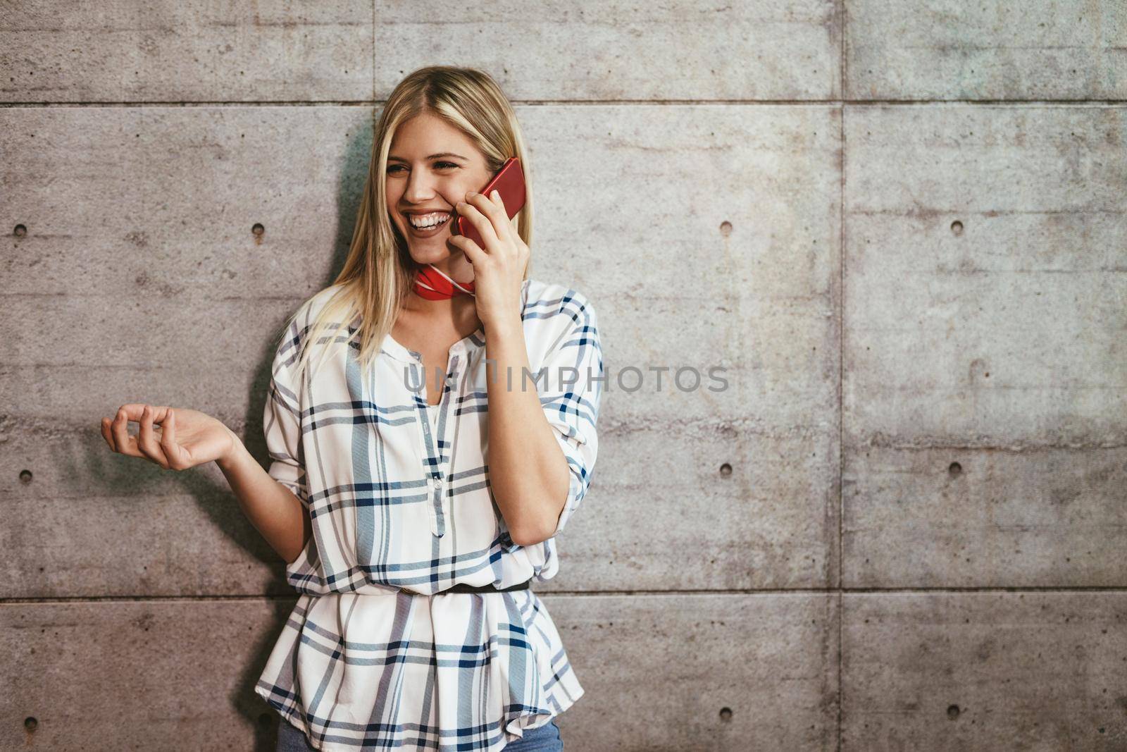 Young beautiful successful female entrepreneur talking on a smart phone in front of a concrete wall.