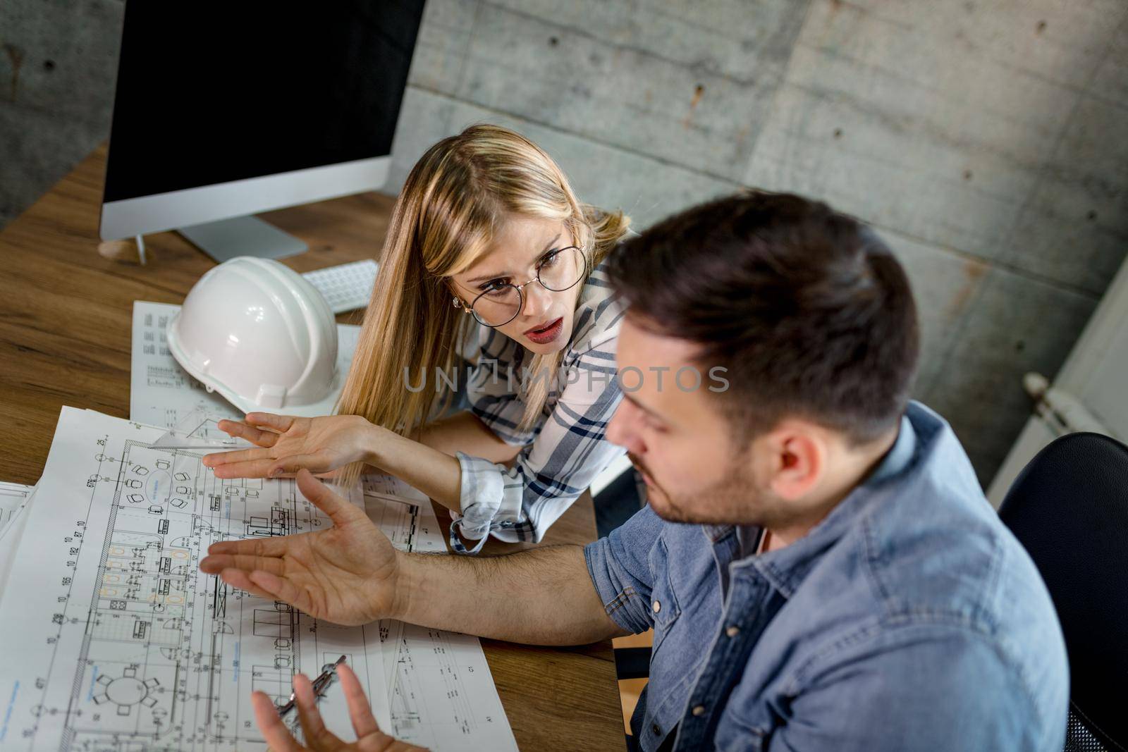 Young worried architect colleagues talking and analyzing blueprints while working on a new project at the office.