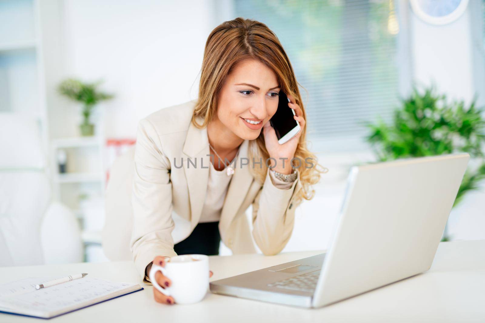 Executive business woman making call while managing her small business, holding cup of a coffee.