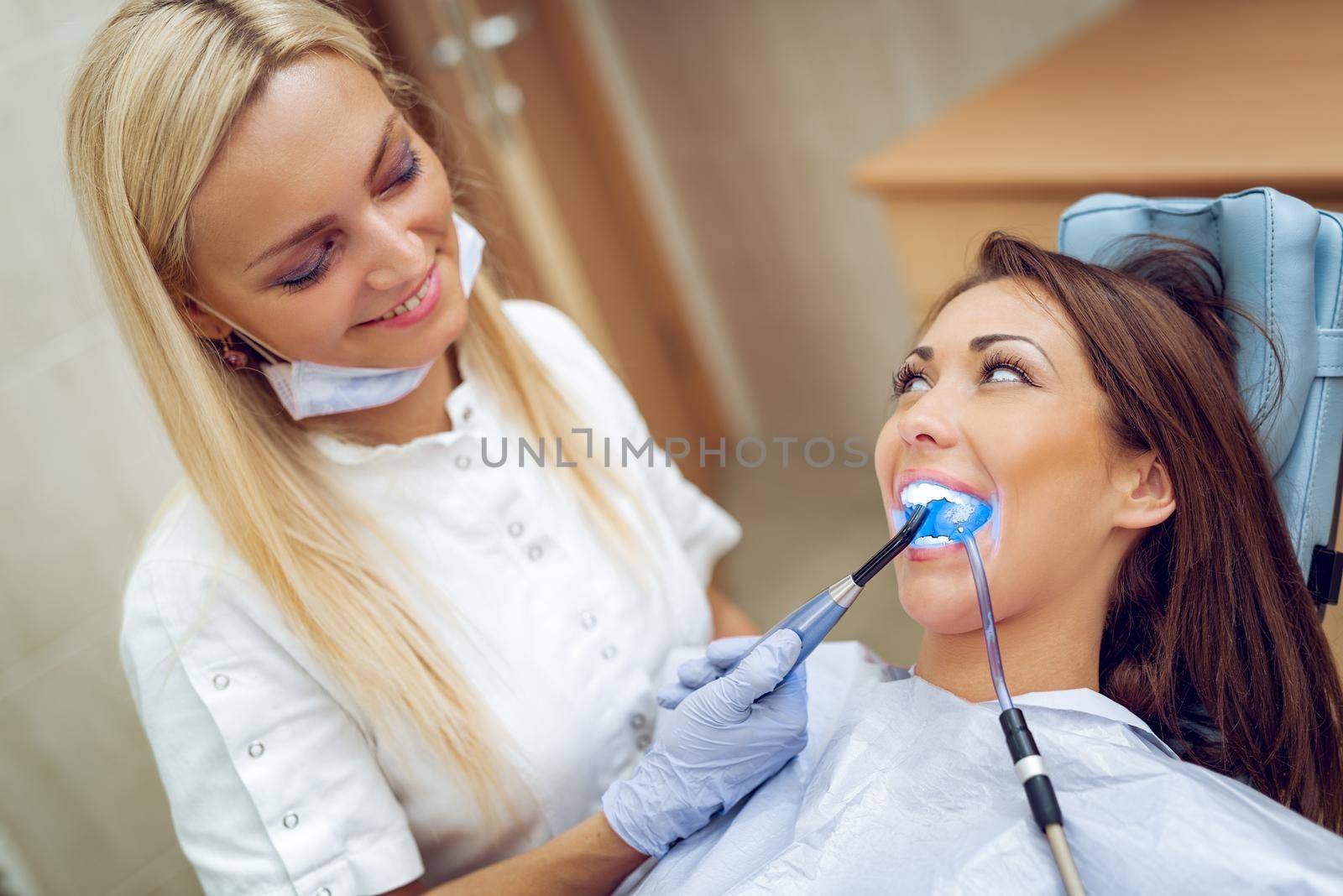 Beautiful young smiling woman at visit in the dentist office and dentist finishing repair tooth with dental curing UV lamp. 