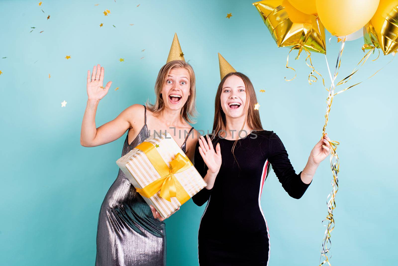 Birthday party. Two young women in birthday hats holding balloons celebrating birthday over blue background