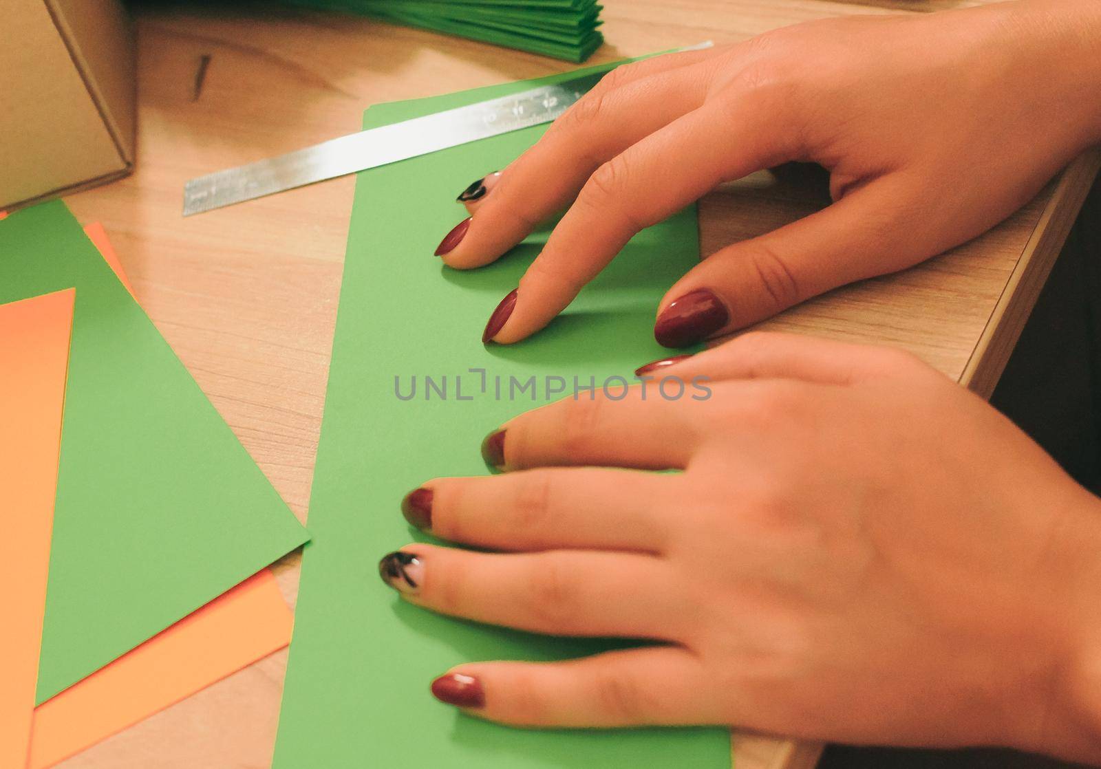 In the foreground, a girl prepares blanks for an origami fan, sheets of colored paper, scissors on a wooden table. Several blanks for a fan. Template for design, advertising or text.