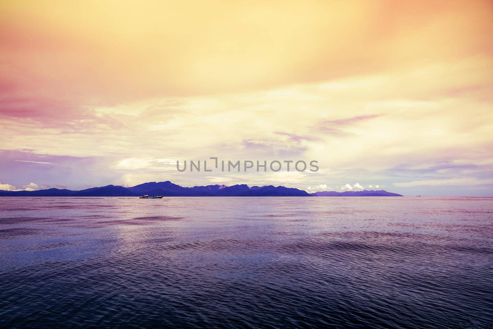 Local passenger boat are sailing on the water surface in the sea with a silhouette of the island in the background. under the bright red yellow sky during the sunset at Pak Bara bay, Satun, Thailand