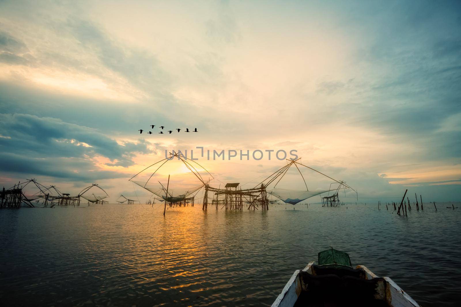 Beautiful nature landscape golden light of the morning sky at sunrise with flock of birds are flying, native fishing tool and prow, rural lifestyle at Pakpra canal, Baan Pak Pra, Phatthalung, Thailand