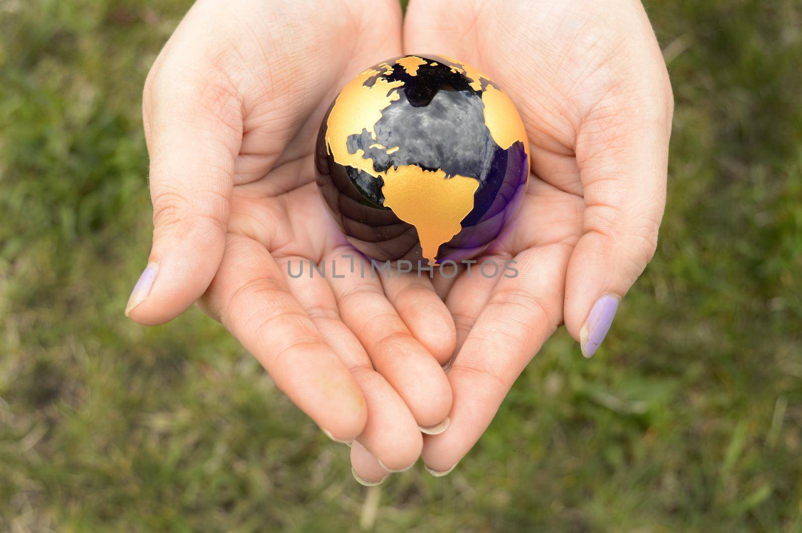 The Earth Globe is safely held inside the palm of a womans hands overtop of a grass area.