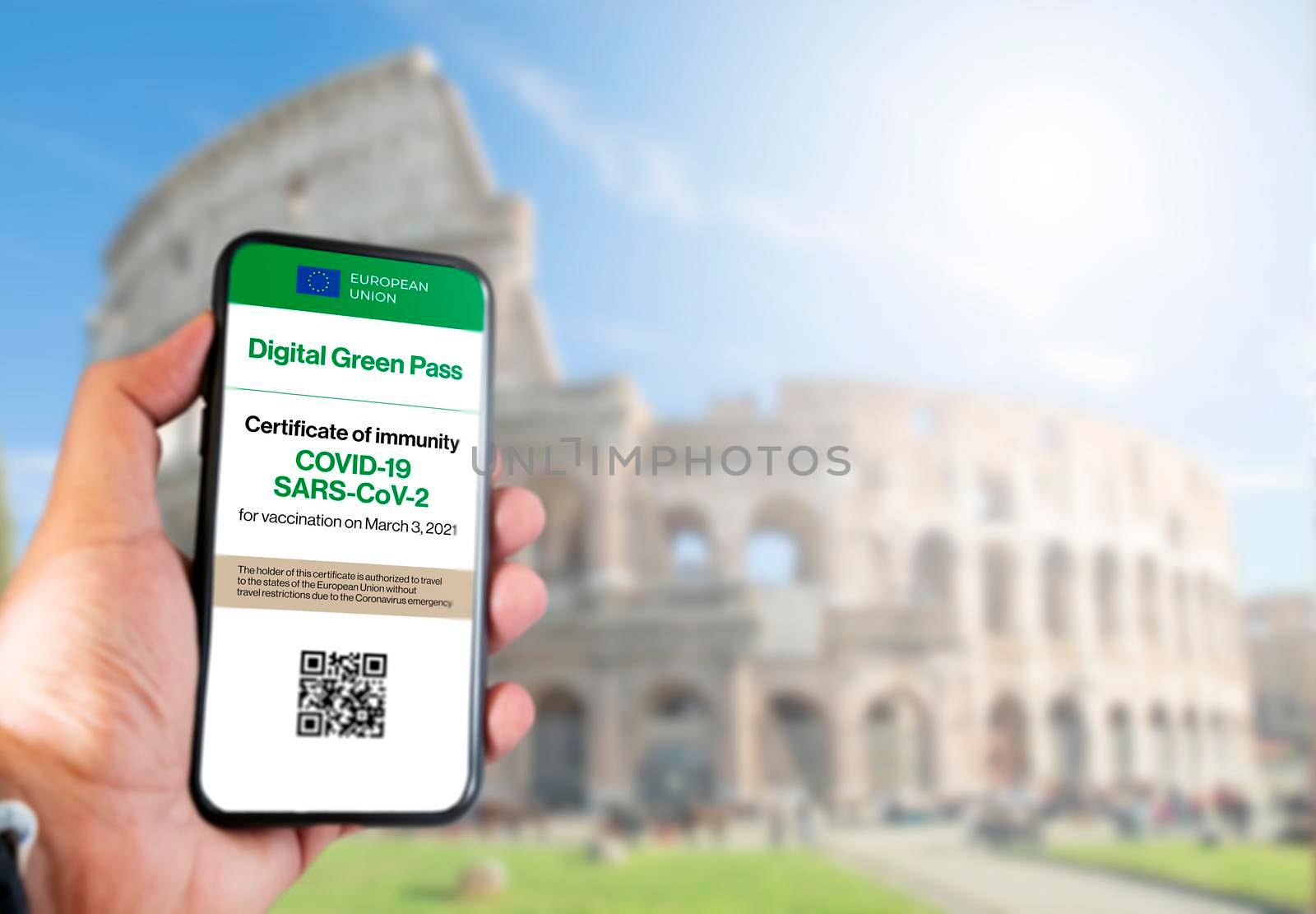The digital green pass of the european union with the QR code on the screen of a mobile held by a hand with blurred colosseum in the background. Immunity from Covid-19. Travel without restrictions.