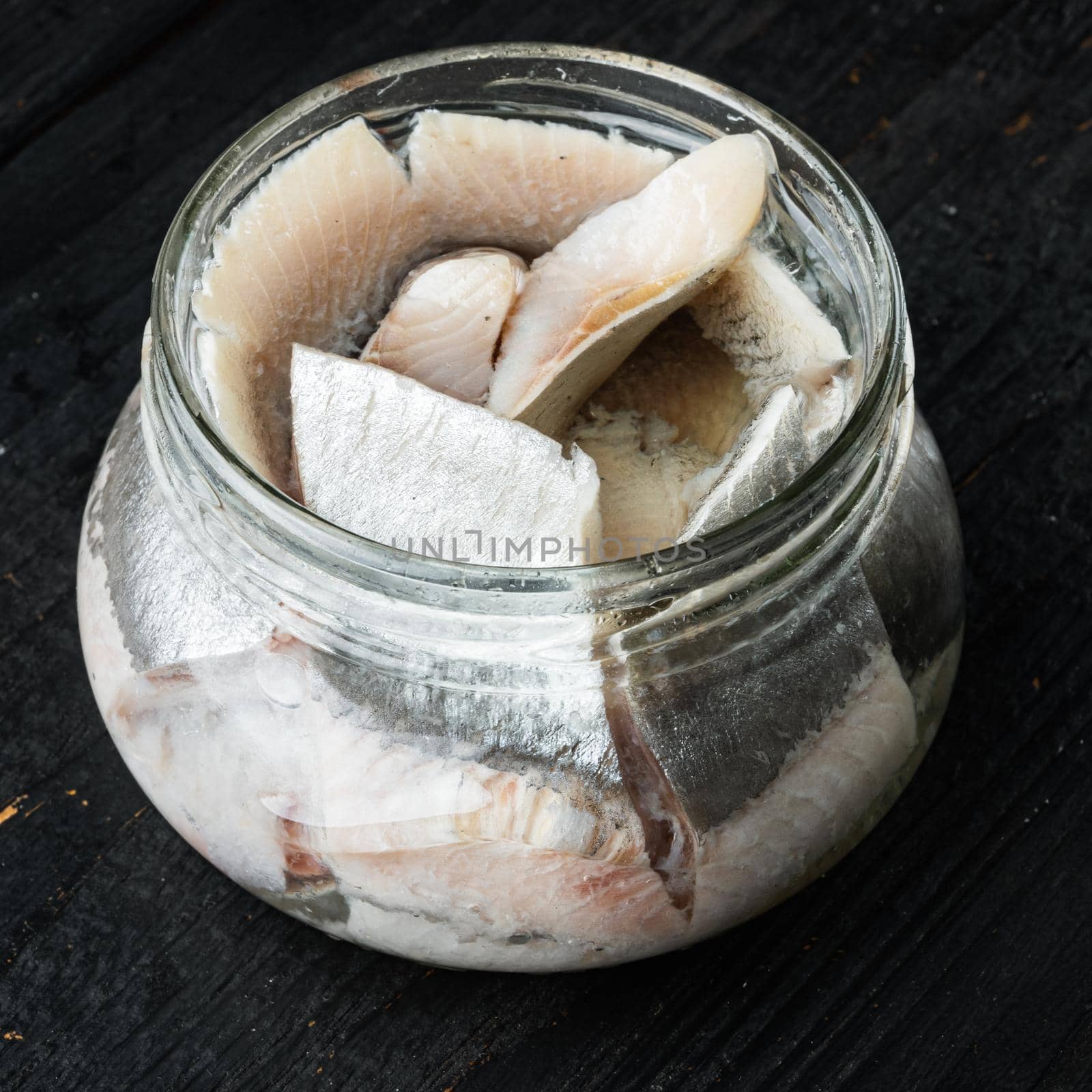 Pickled herring set, in glass jar, on black wooden table background, square format
