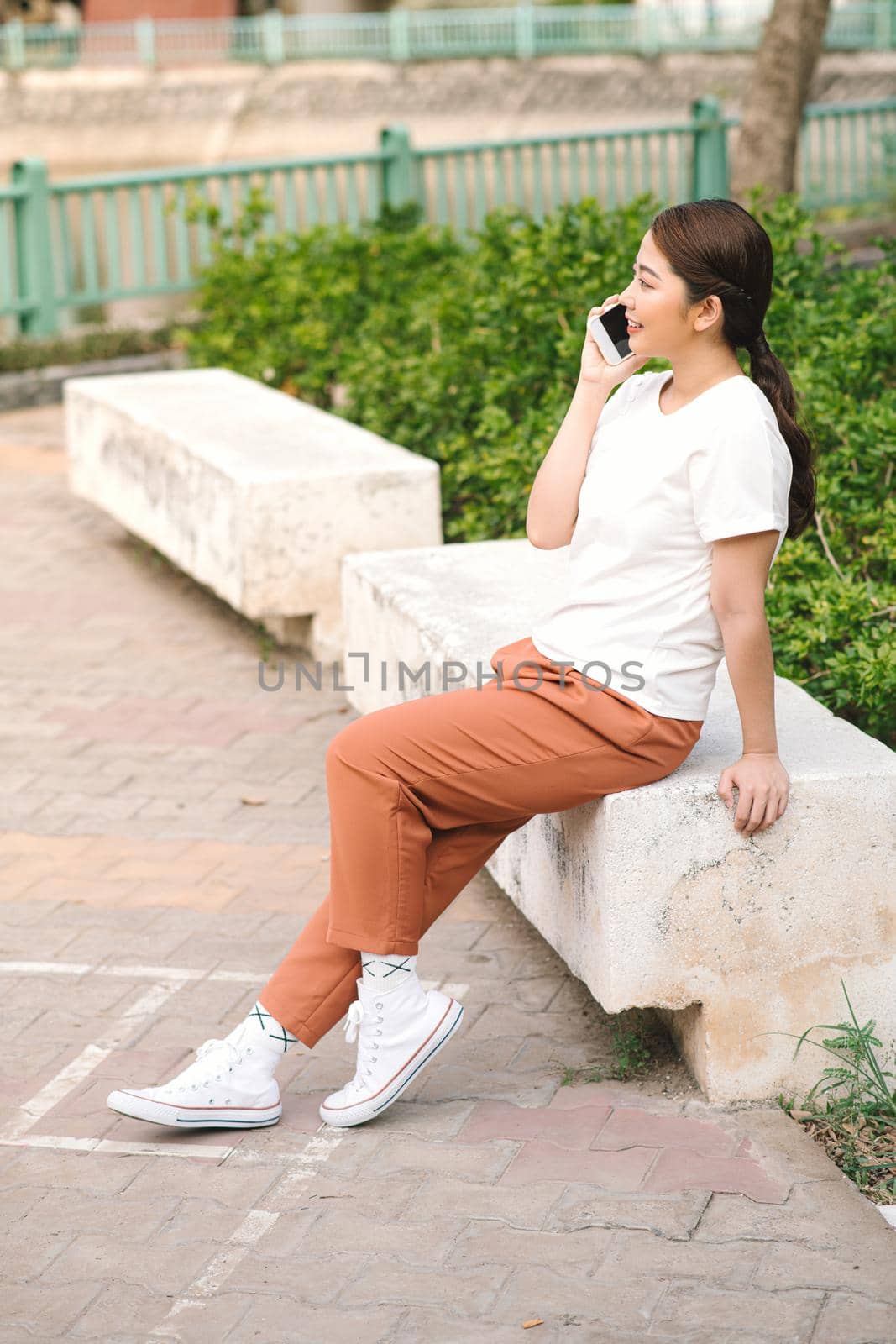 Beautiful young asian girl talking at the cell phone at summer green park