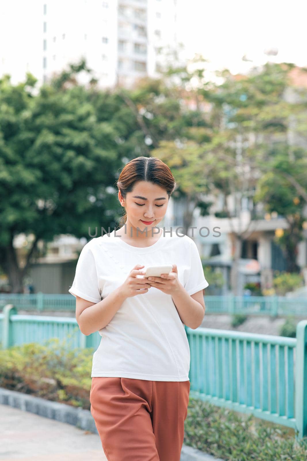 Young fashionable woman uses smartphone walking in summer park.