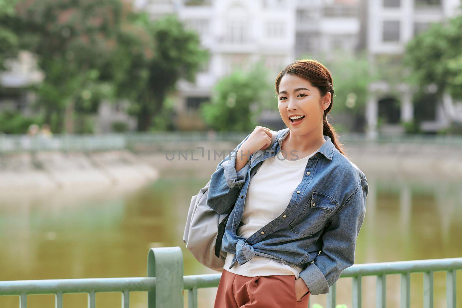 Portrait of a smiling young girl with backpack standing outdoors  by makidotvn