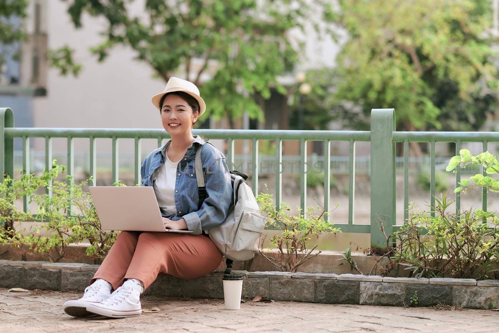 Smiling young girl making notes in notepad while sitting outdoors with laptop computer