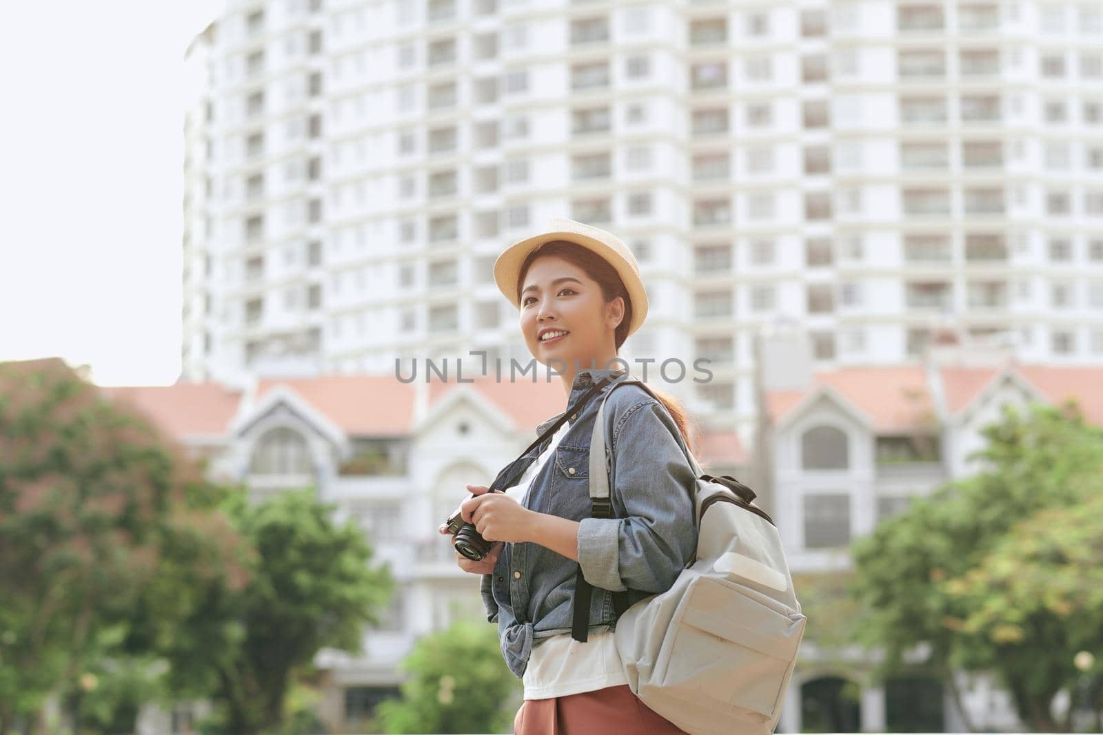 Young beautiful Asian backpack traveler woman using digital compact camera and smile, looking at copy space. 