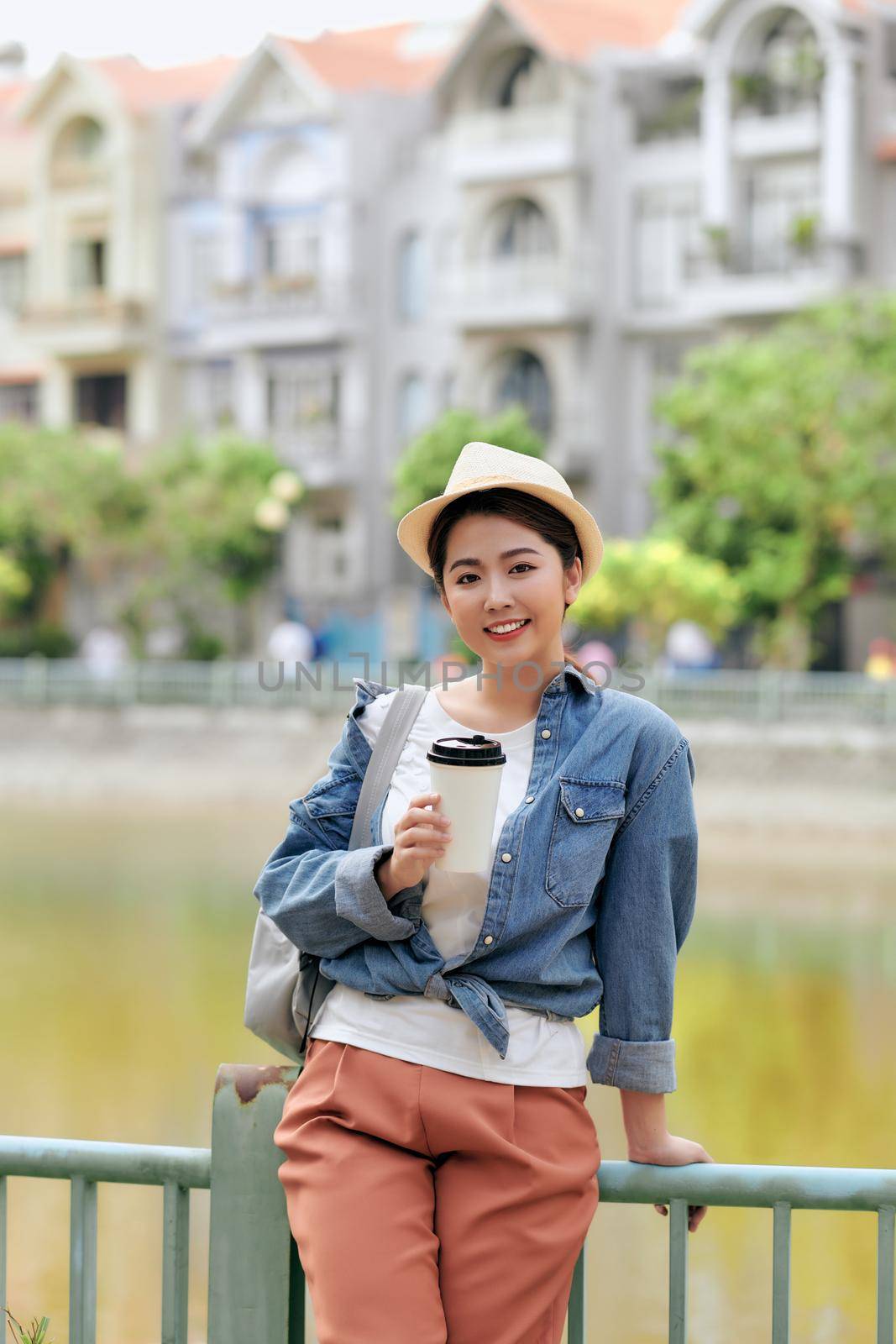 Attractive cheerful trendy girl in stylish denim jacket drinks takeaway coffee or tea outdoors