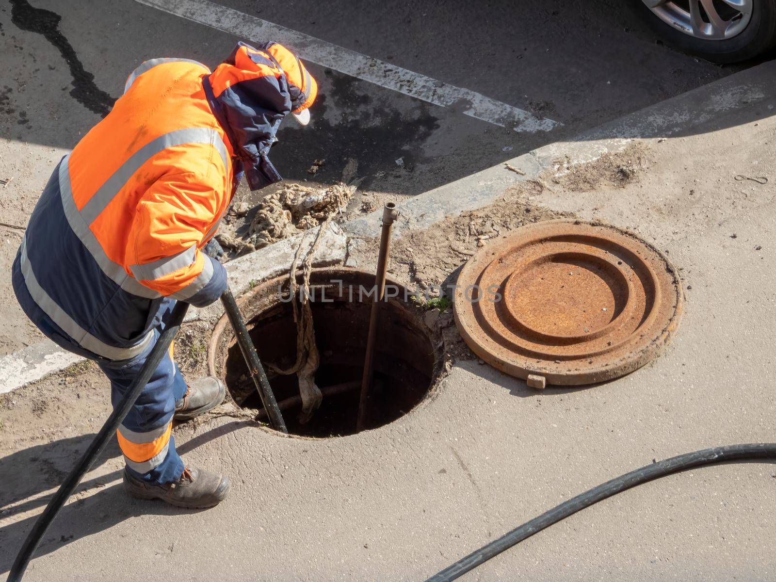 Worker over the open sewer hatch on a street. Repair of sewage, underground utilities, water supply system, water pipe accident