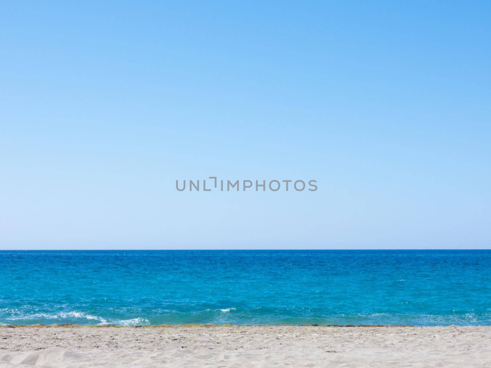 Summer mediterranean beach background. Horizon with calm sea, clear sky and grey sand