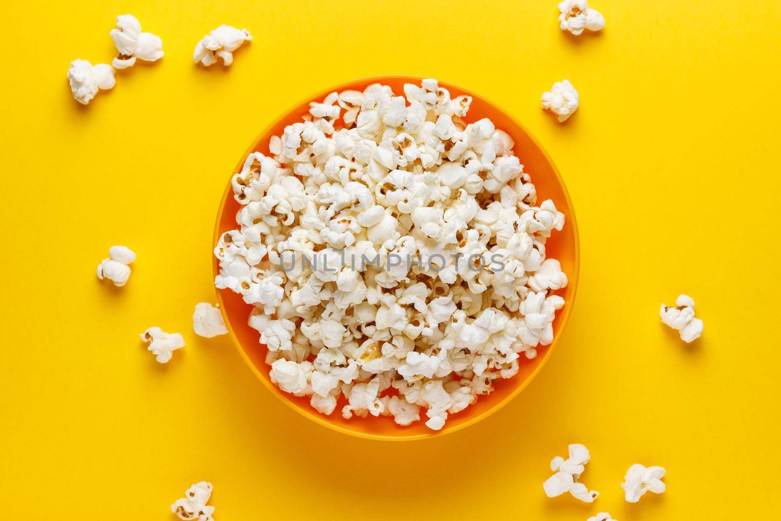 Popcorn in an orange bowl on yellow background. Horizontal image. Top view.