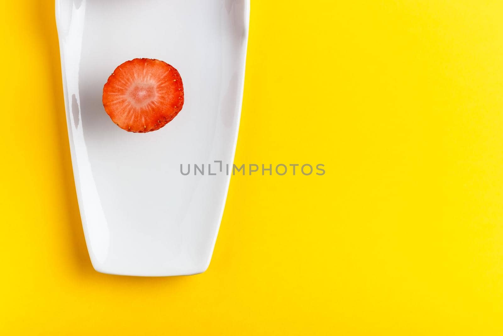 Slice of fresh strawberry in a white dish on yellow background. Horizontal image seen from above.