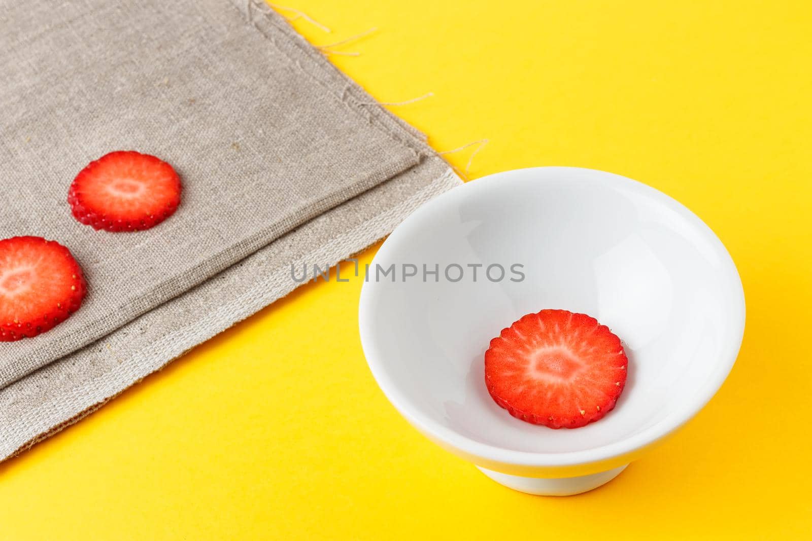 Three slices of fresh strawberries in a round white plate on yellow background and sackcloth. Horizontal image.