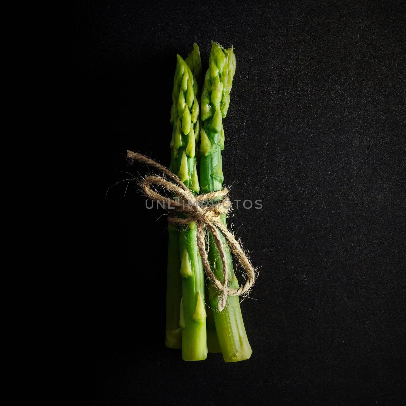 Asparagus. Bunch of fresh green asparagus tied on black background. Healthy vegetarian food. Square image