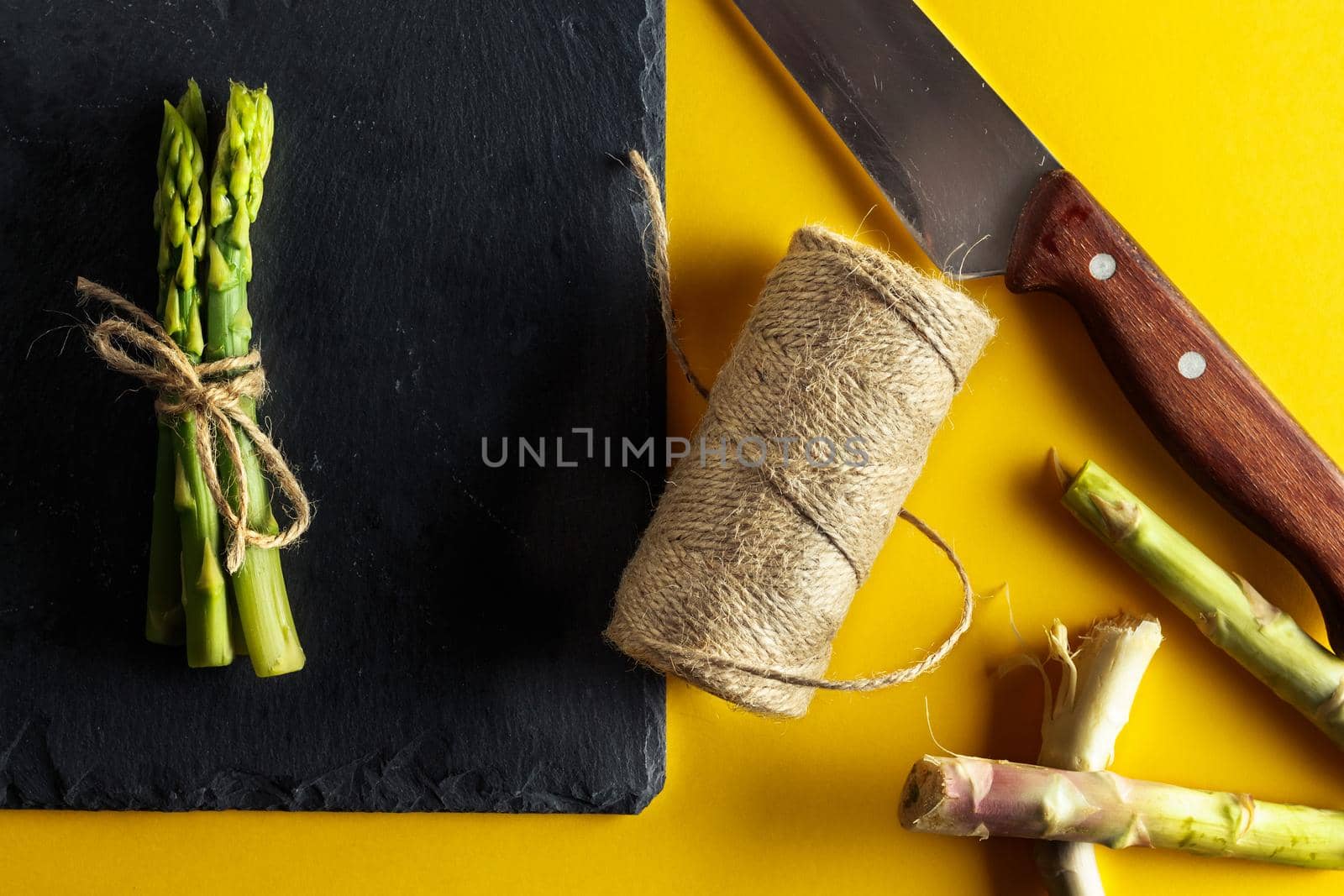 Asparagus. Bunch of fresh asparagus tied on a plate of slate with a knife, a roll of rope and slices of asparagus cut on yellow background .. Healthy vegetarian food. Horizontal image