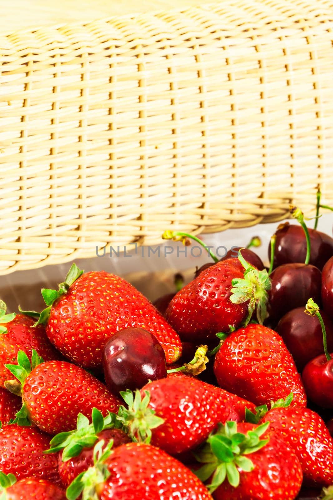 Strawberries and cherries in a wicker basket in the background. Vertical image.