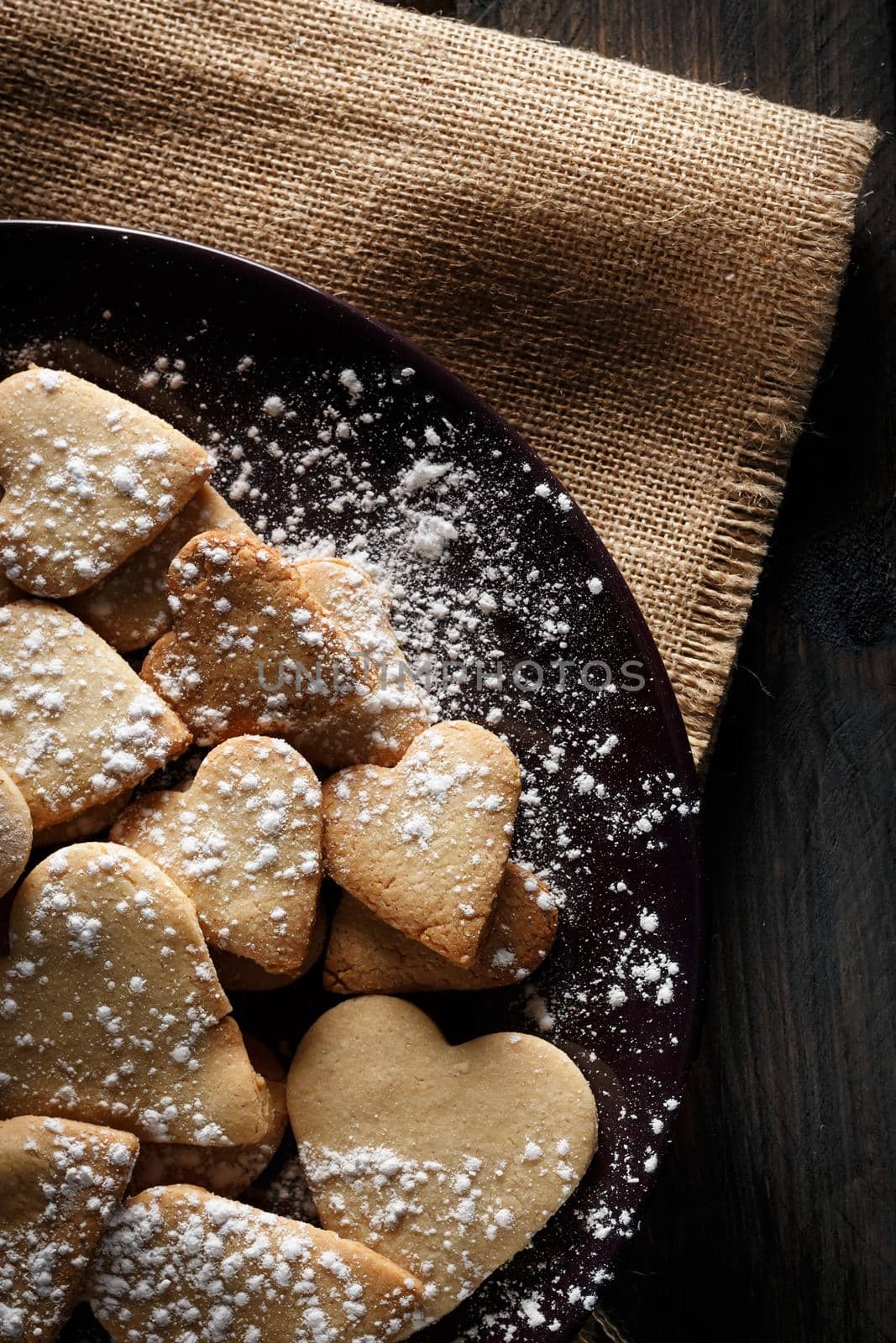 Delicious home-made heart-shaped cookies sprinkled with icing sugar on sackcloth and wooden boards. Vertical image seen from above.