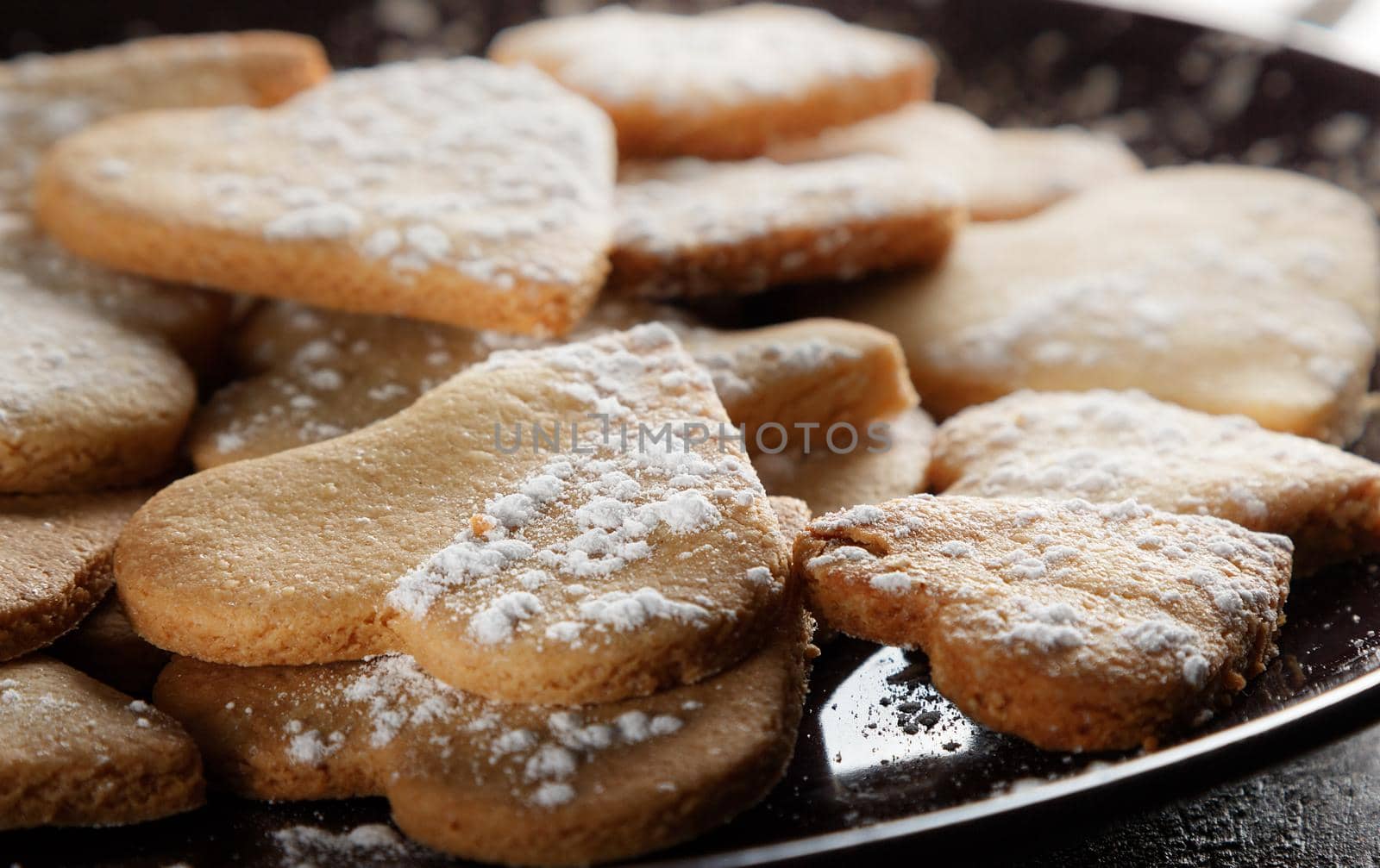 Delicious home-made heart-shaped cookies sprinkled with icing sugar on sackcloth and wooden boards. Horizontal image seen against backlight.