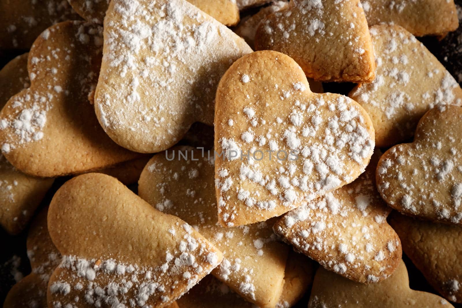 Delicious home-made heart-shaped cookies sprinkled with icing sugar on sackcloth and wooden boards. Horizontal image seen from above.