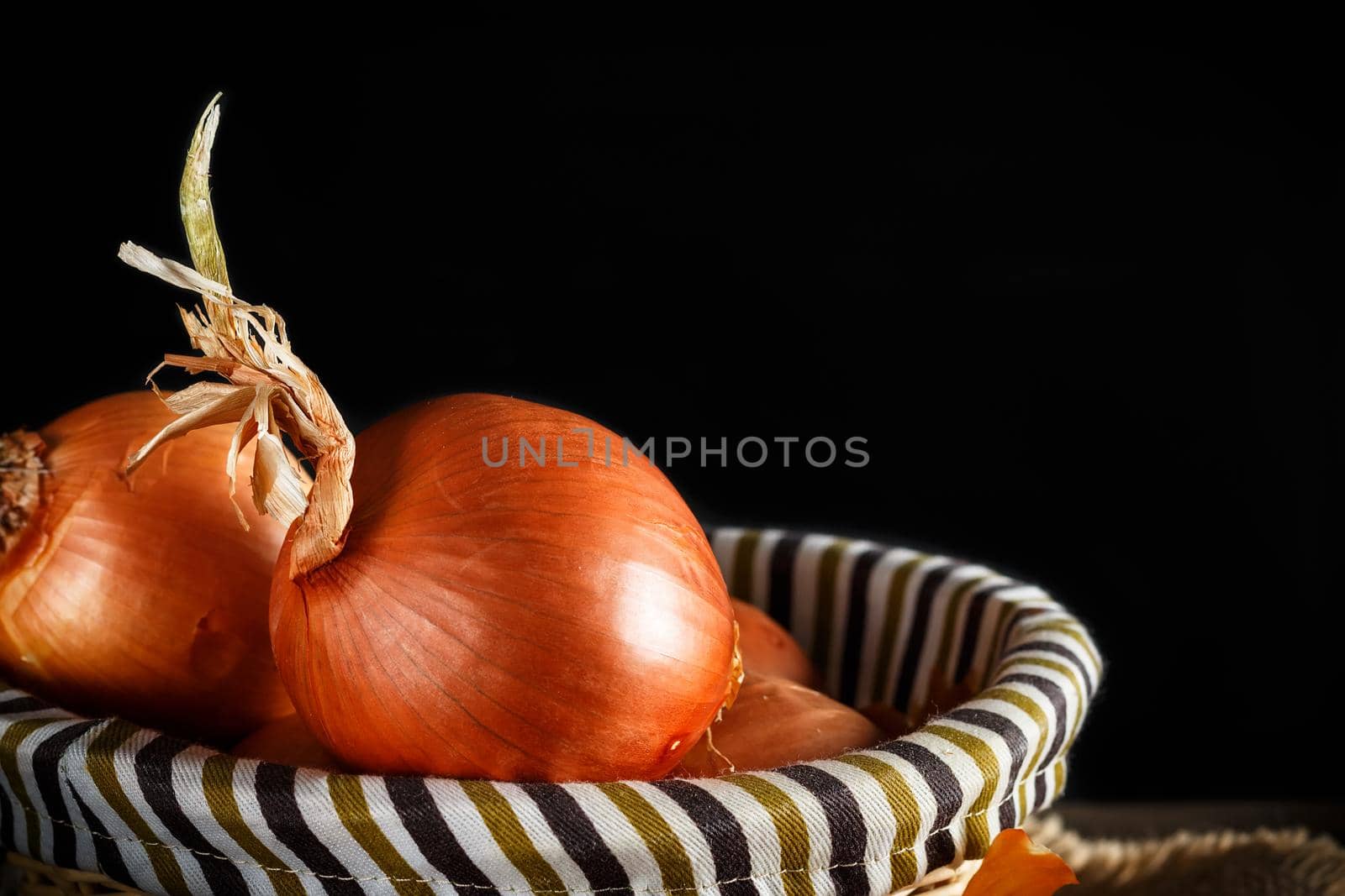 Still life of onions with wicker basket with black background. Rustic style. Horizontal image.