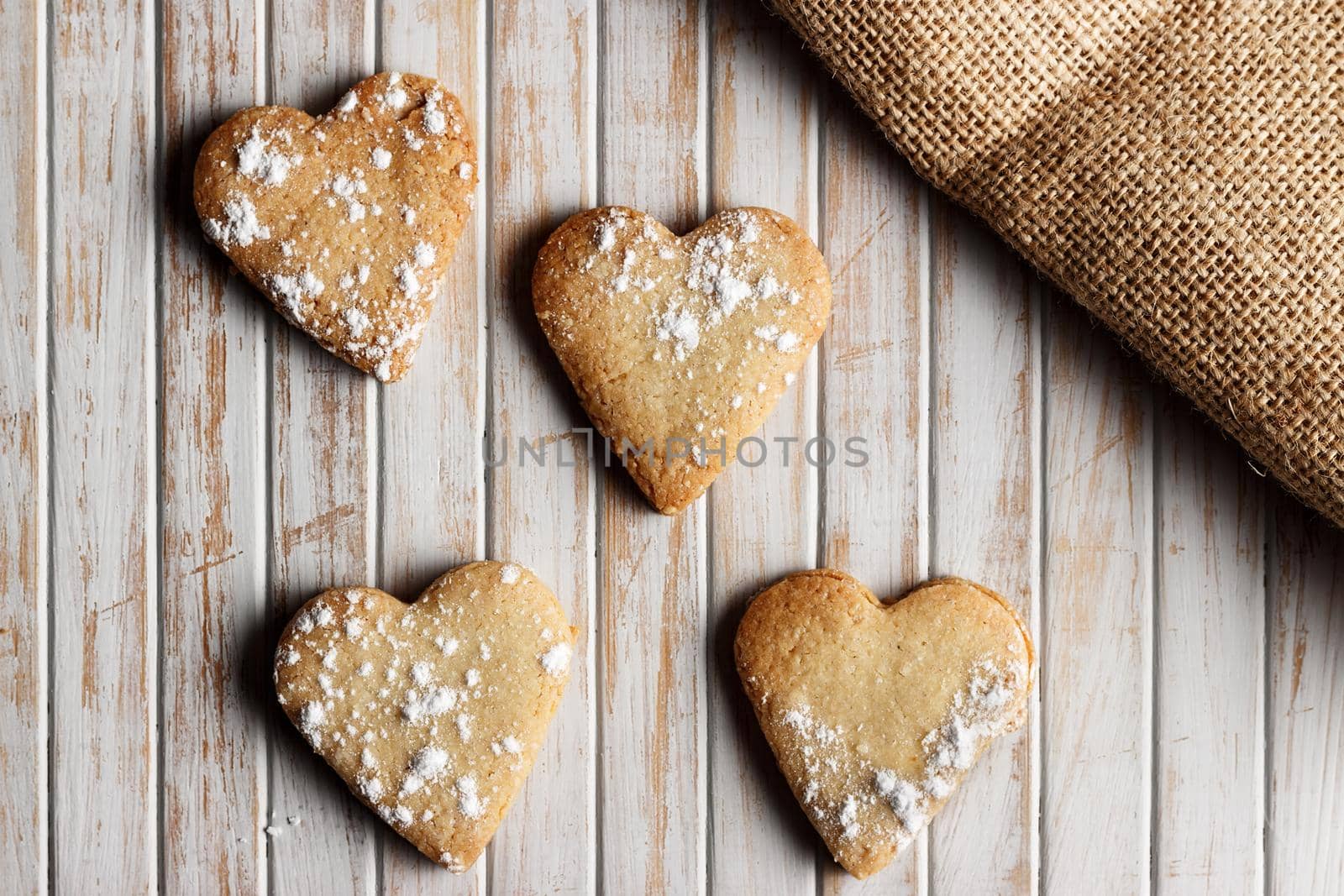 Delicious home-made heart-shaped cookies sprinkled with icing sugar in a wooden board. Horizontal image seen from above. 
