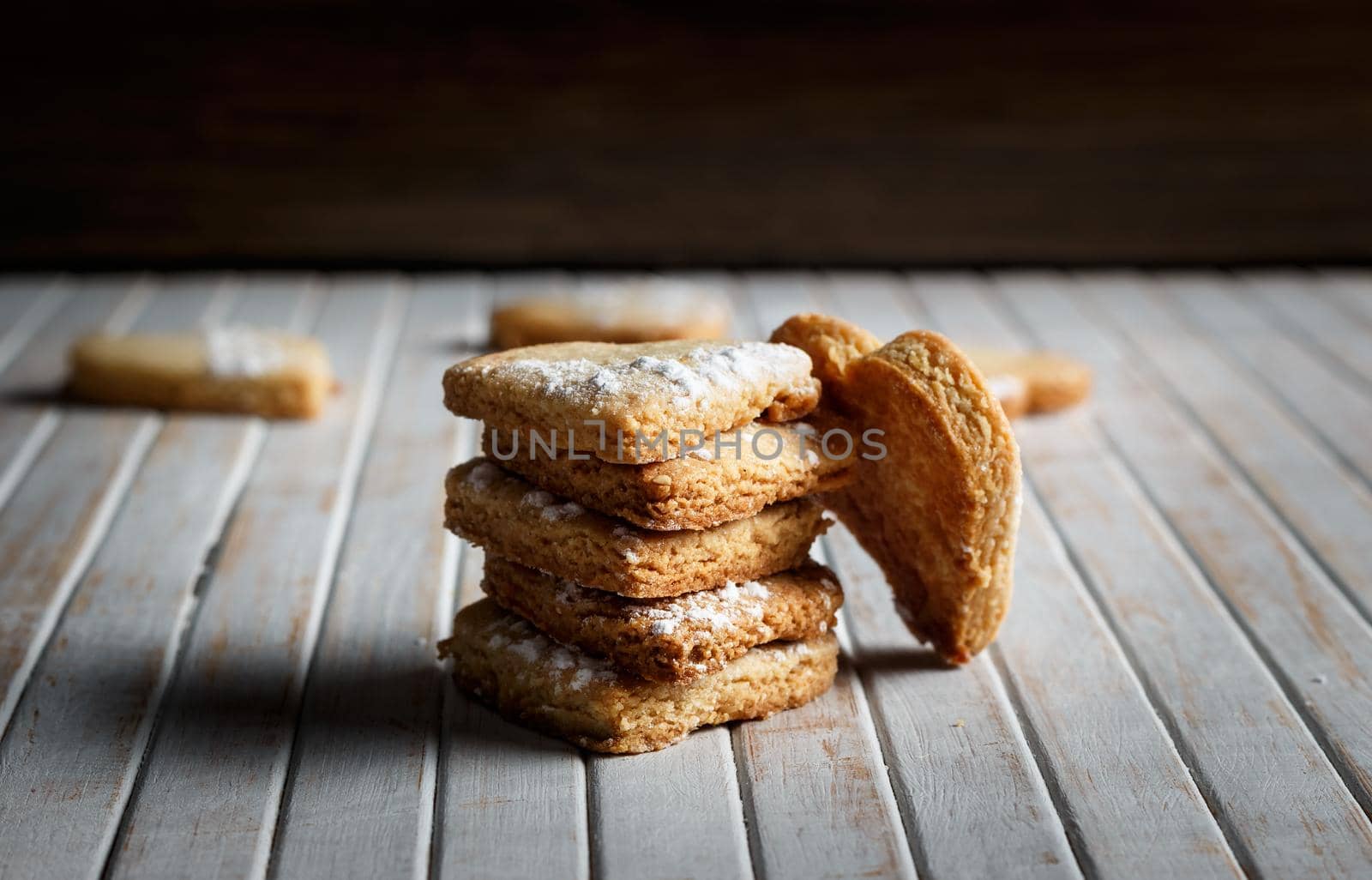 Delicious home-made heart-shaped cookies sprinkled with icing sugar in a wooden board. Horizontal image. Dark moody style.