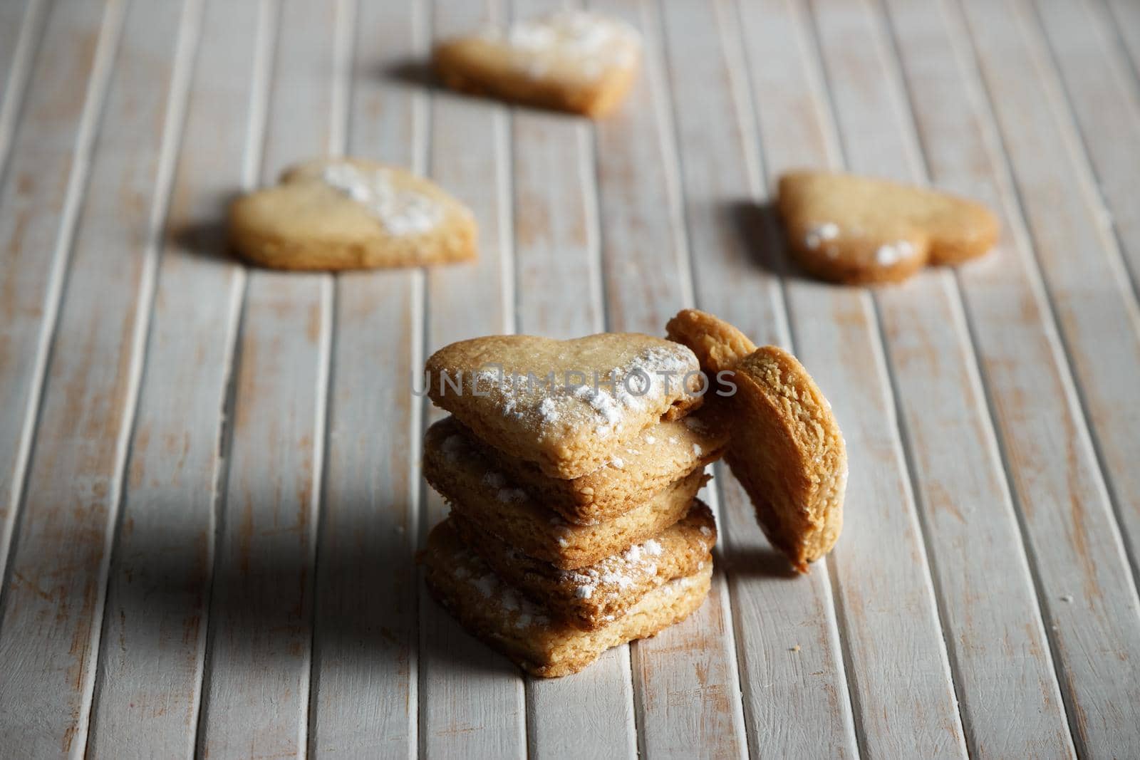 Delicious home-made heart-shaped cookies sprinkled with icing sugar in a wooden board. Horizontal image. Dark moody style.