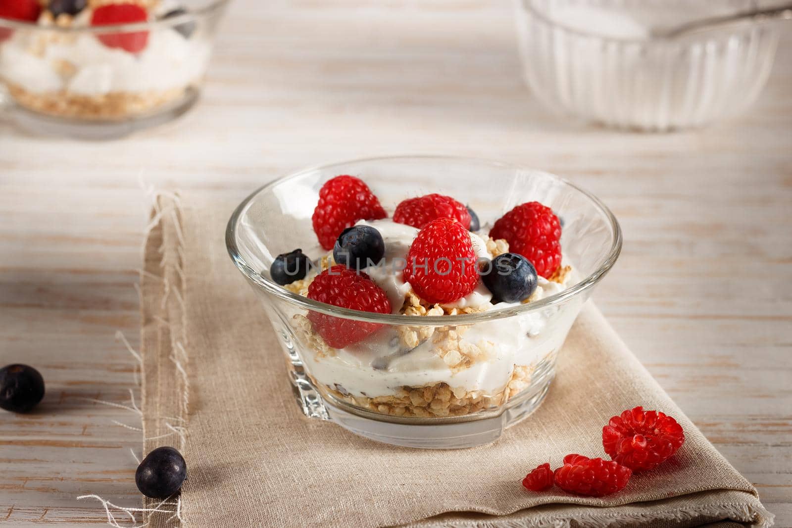 Raspberries, blueberries, cereals and yogurt in a glass bowl on sackcloth and wooden slats. Healthy breakfast for a healthy life. Horizontal image.