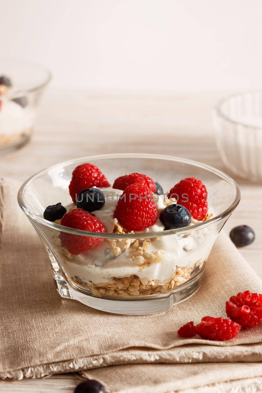 Raspberries, blueberries, cereals and yogurt in a glass bowl on sackcloth and wooden slats. Healthy breakfast for a healthy life. Vertical image.