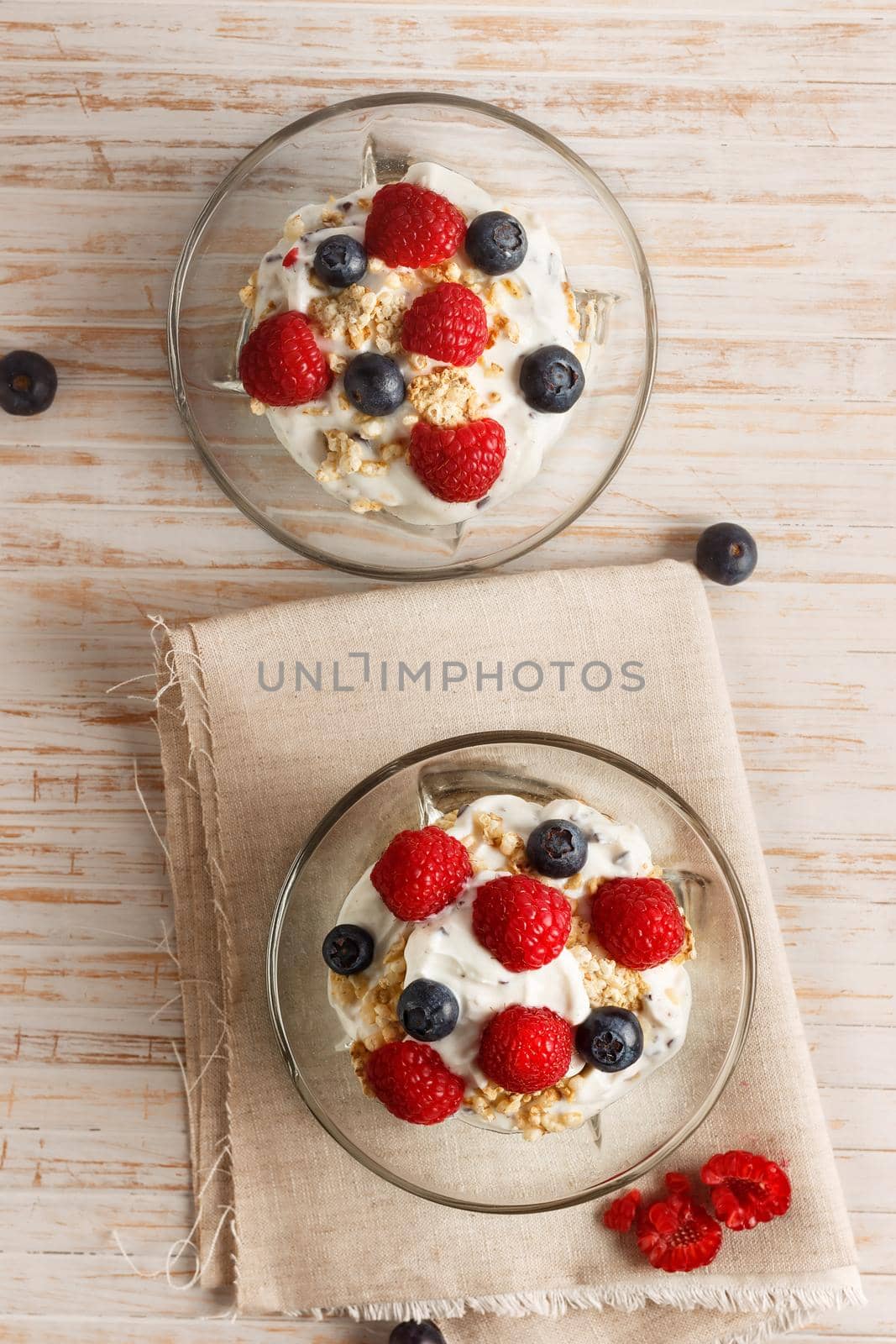 Raspberries, blueberries, cereals and yogurt in a glass bowl on sackcloth and wooden slats. Healthy breakfast for a healthy life. Vertical image view from above.