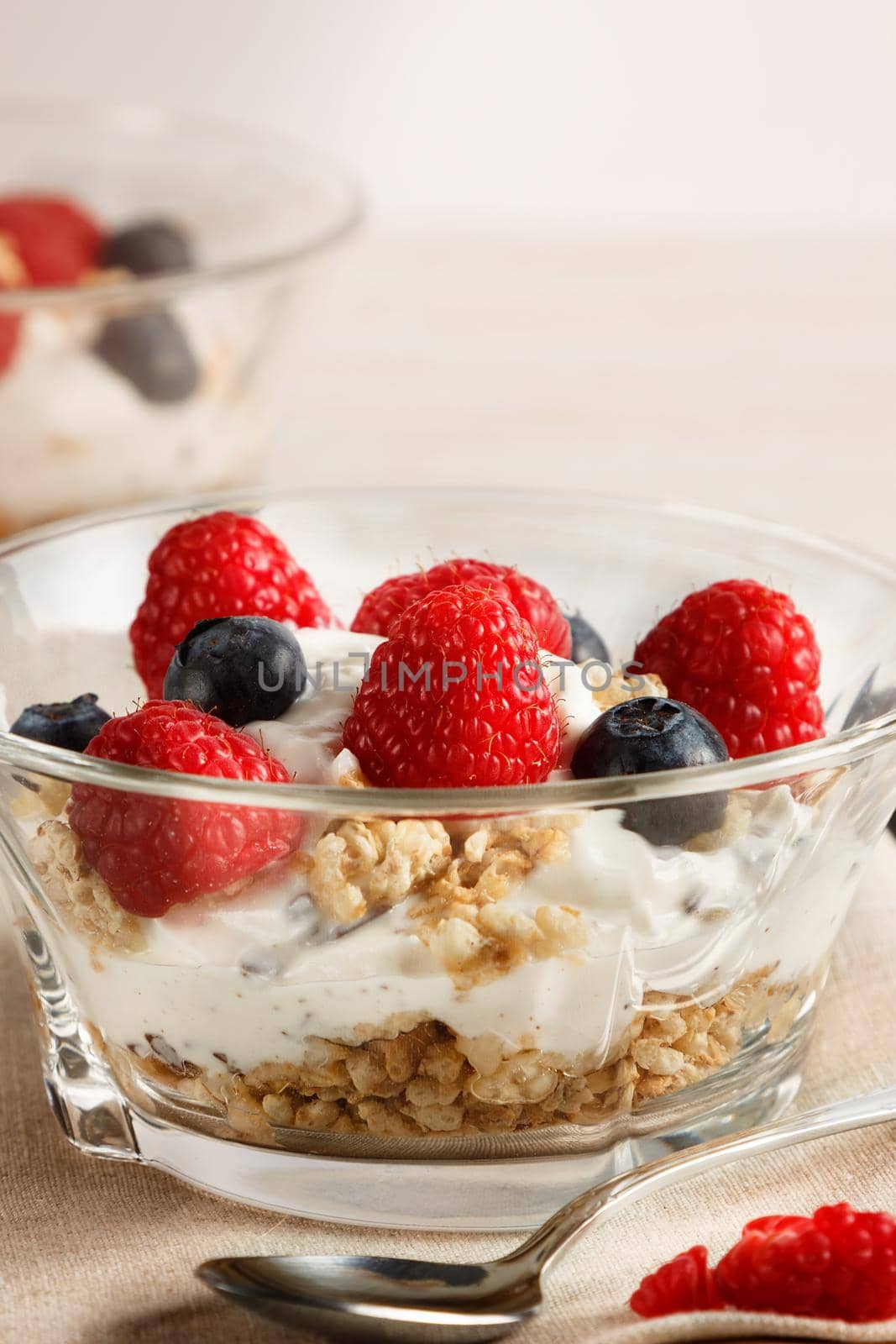 Raspberries, blueberries, cereals and yogurt in a glass bowl on sackcloth and wooden slats. Healthy breakfast for a healthy life. Vertical image.