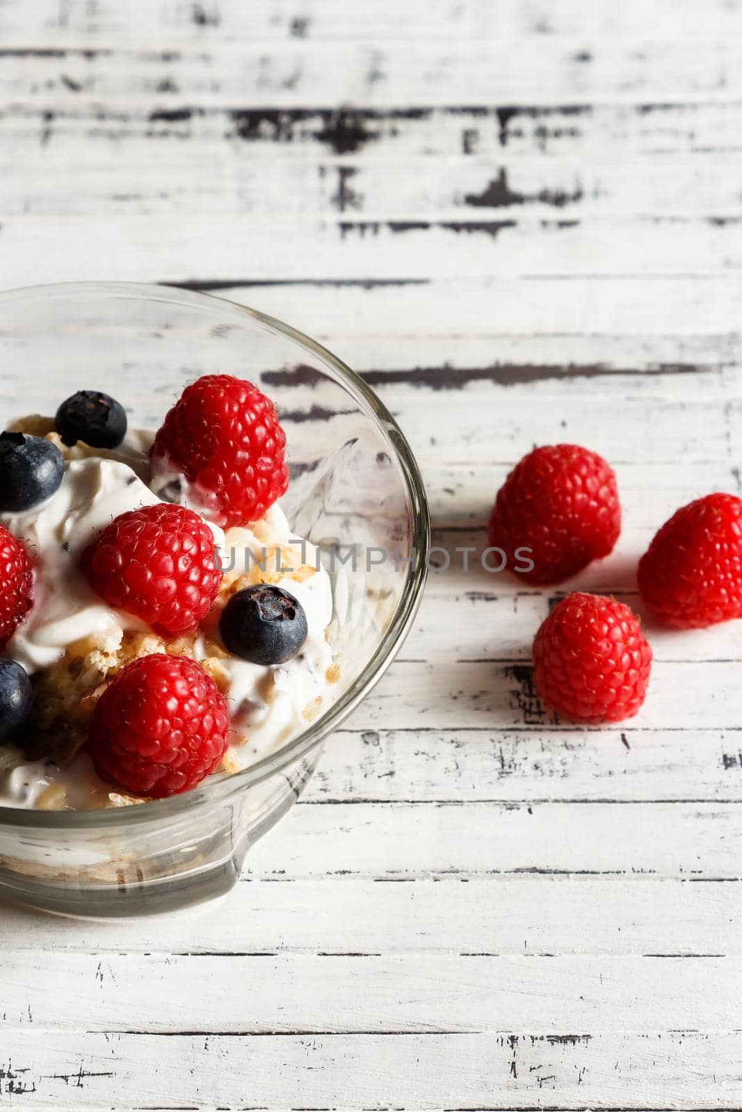 Raspberries, blueberries, cereals and yogurt in a glass bowl on wooden slats. Healthy breakfast for a healthy life. Vertical image.