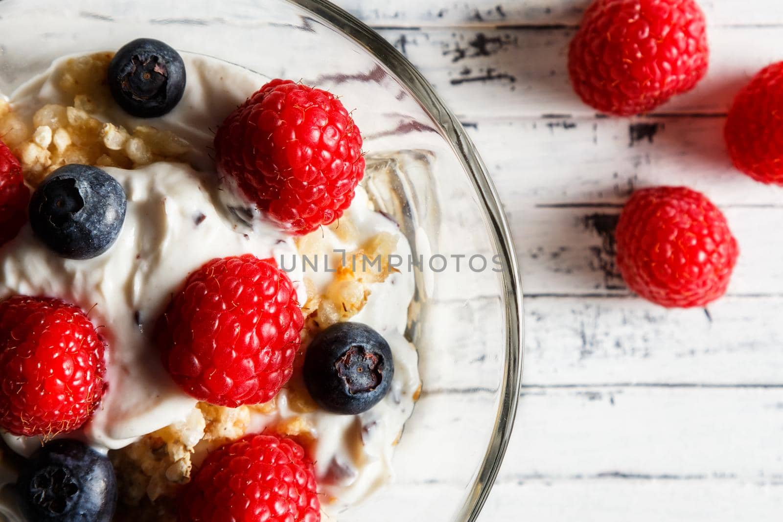Raspberries, blueberries, cereals and yogurt in a glass bowl on wooden slats. Healthy breakfast for a healthy life. Horizontal image view from above. Close up.