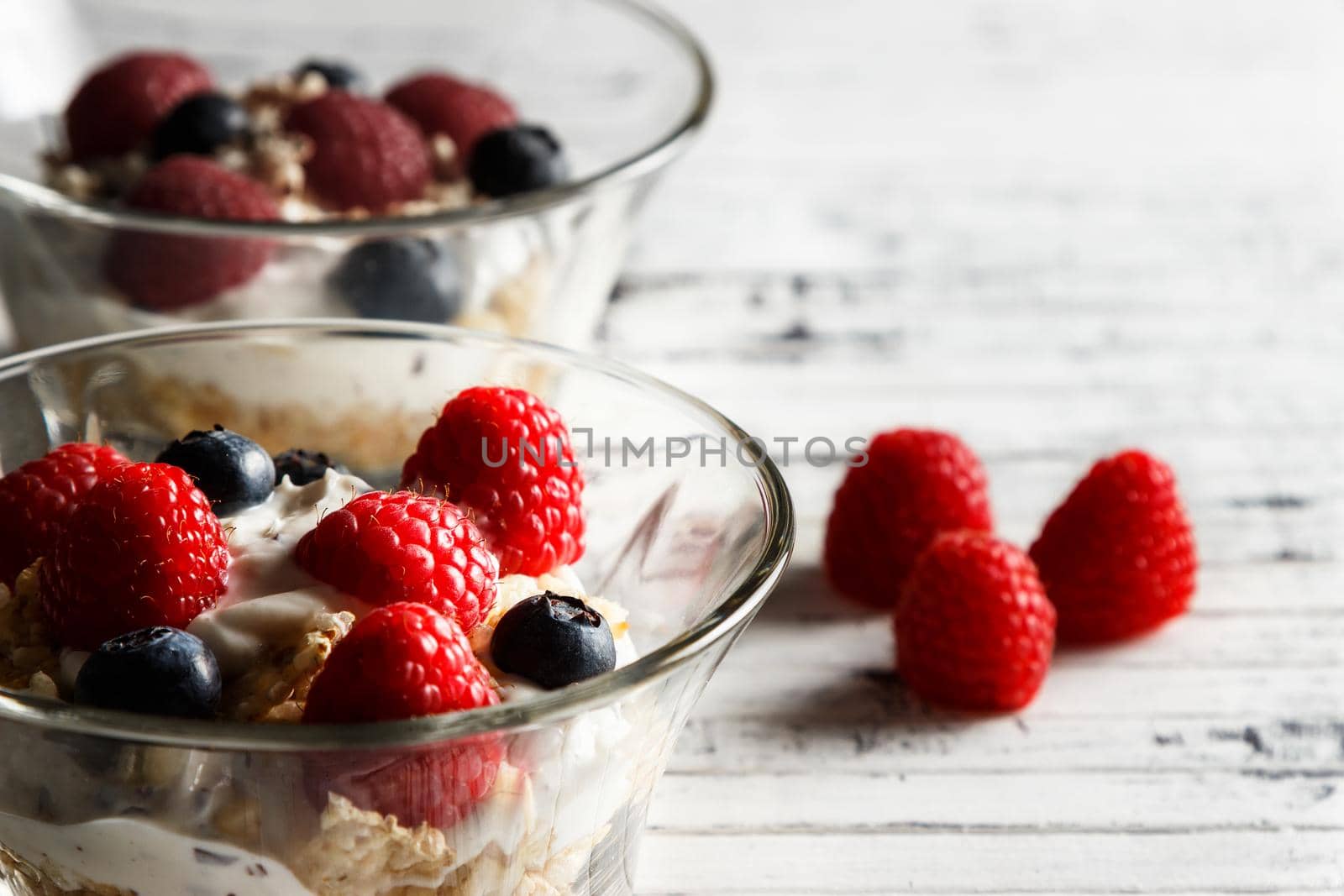 Raspberries, blueberries, cereals and yogurt in a glass bowl on wooden slats. Healthy breakfast for a healthy life. Horizontal image.