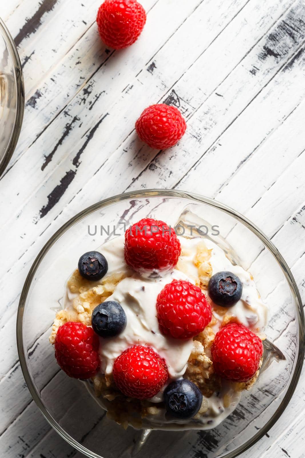 Raspberries, blueberries, cereals and yogurt in a glass bowl on wooden slats. Healthy breakfast for a healthy life. Vertical image view from above.