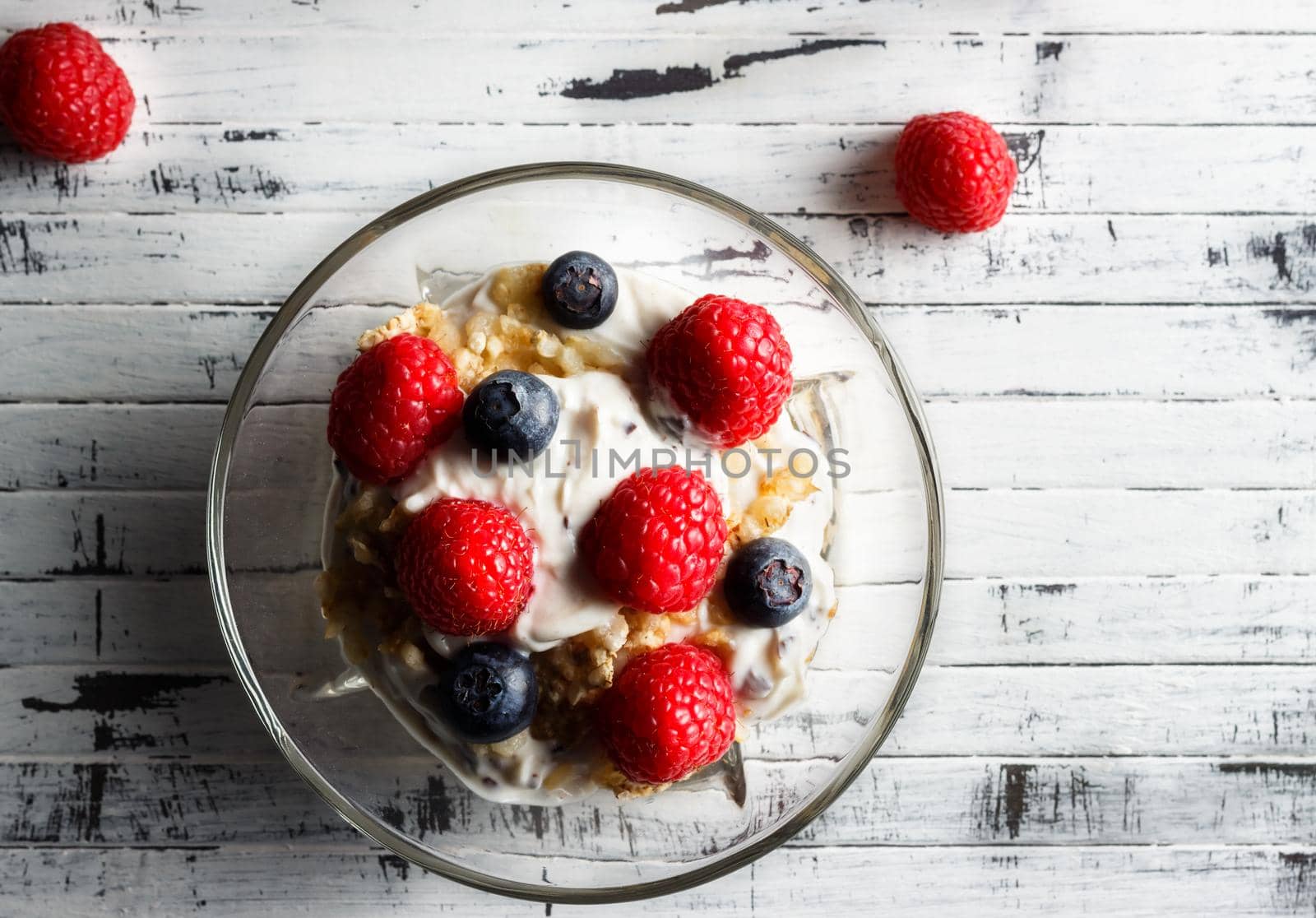 Raspberries, blueberries, cereals and yogurt in a glass bowl on wooden slats. Healthy breakfast for a healthy life. Horizontal image view from above.