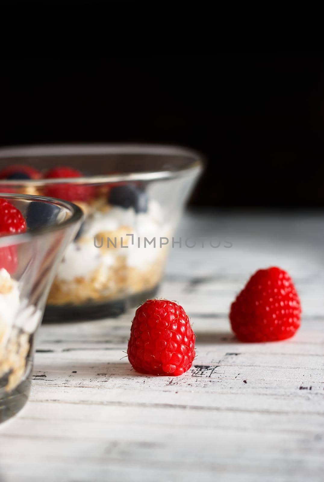 Raspberries, blueberries, cereals and yogurt in a glass bowl on wooden slats. Healthy breakfast for a healthy life. Vertical image.