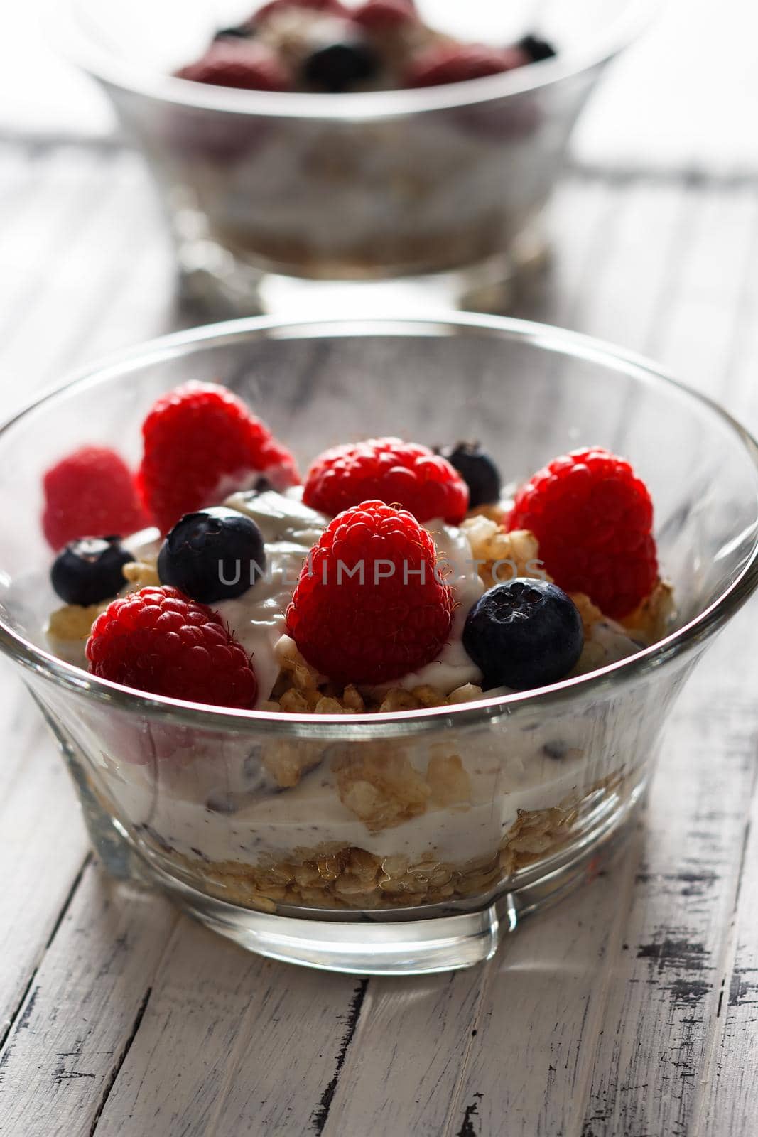 Raspberries, blueberries, cereals and yogurt in a glass bowl on wooden slats. Healthy breakfast for a healthy life. Vertical image.