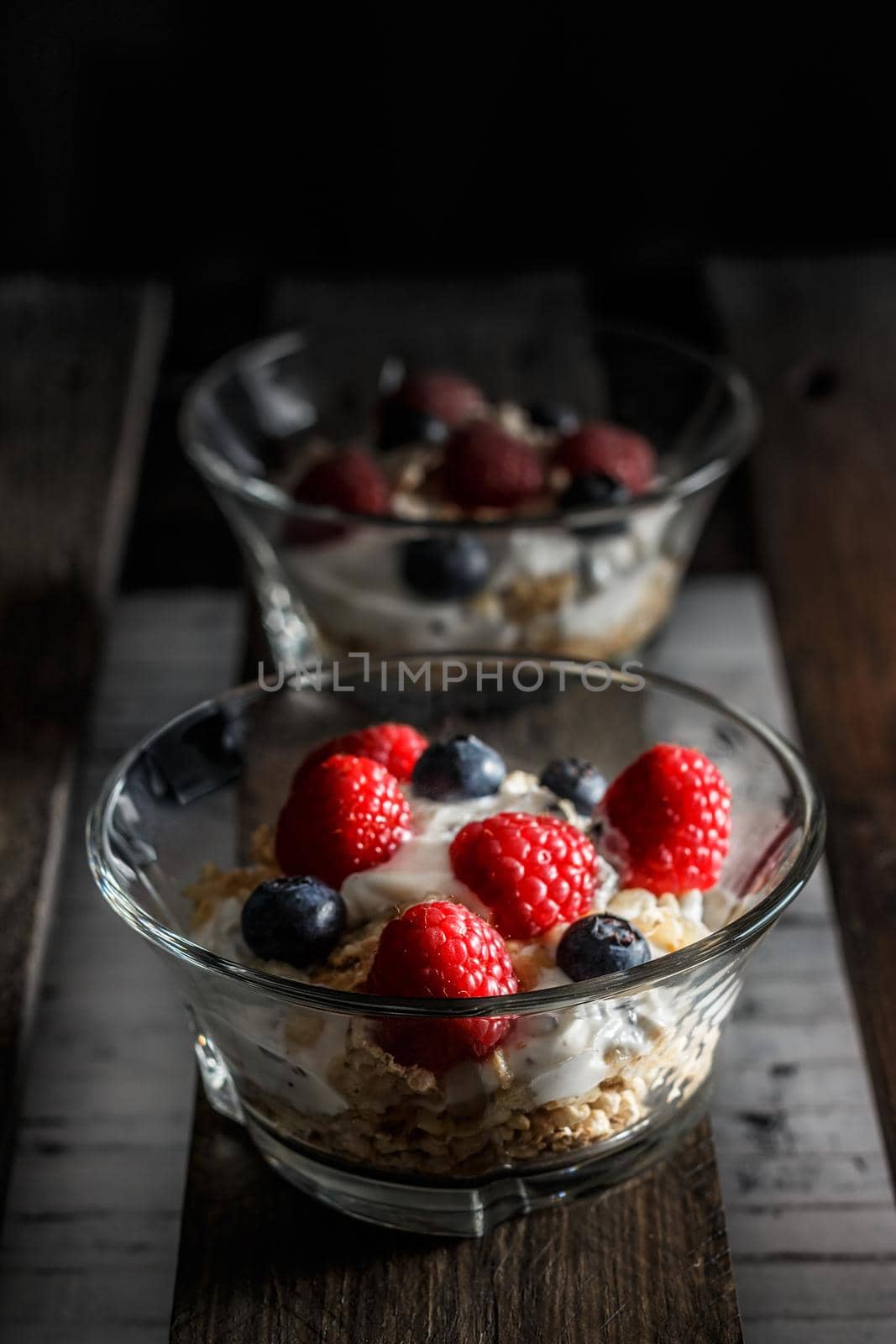 Raspberries, blueberries, cereals and yogurt in a glass bowl on old wooden boards. Healthy breakfast for a healthy life. Vertical image.