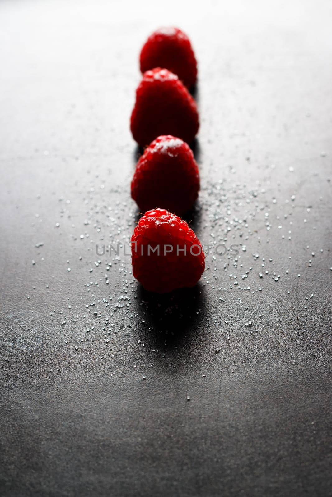 Red raspberries in a row with sugar on top on a black griddle. Backlighting. Vertical image.