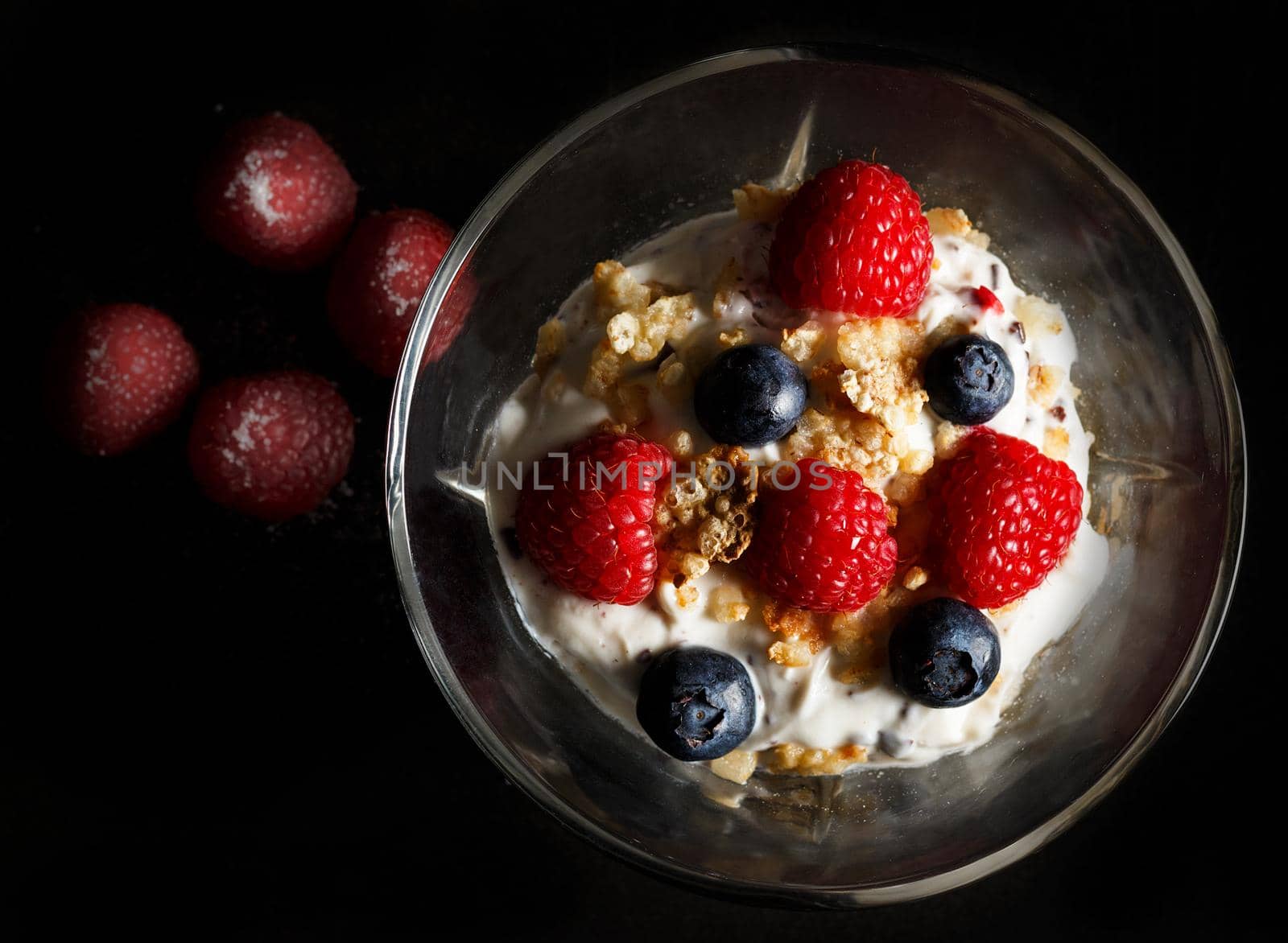 Yogurt bowl with oat flakes, blueberries and raspberries on black background. Healthy breakfast concept. Dark moody style.Top view. Horizontal image.