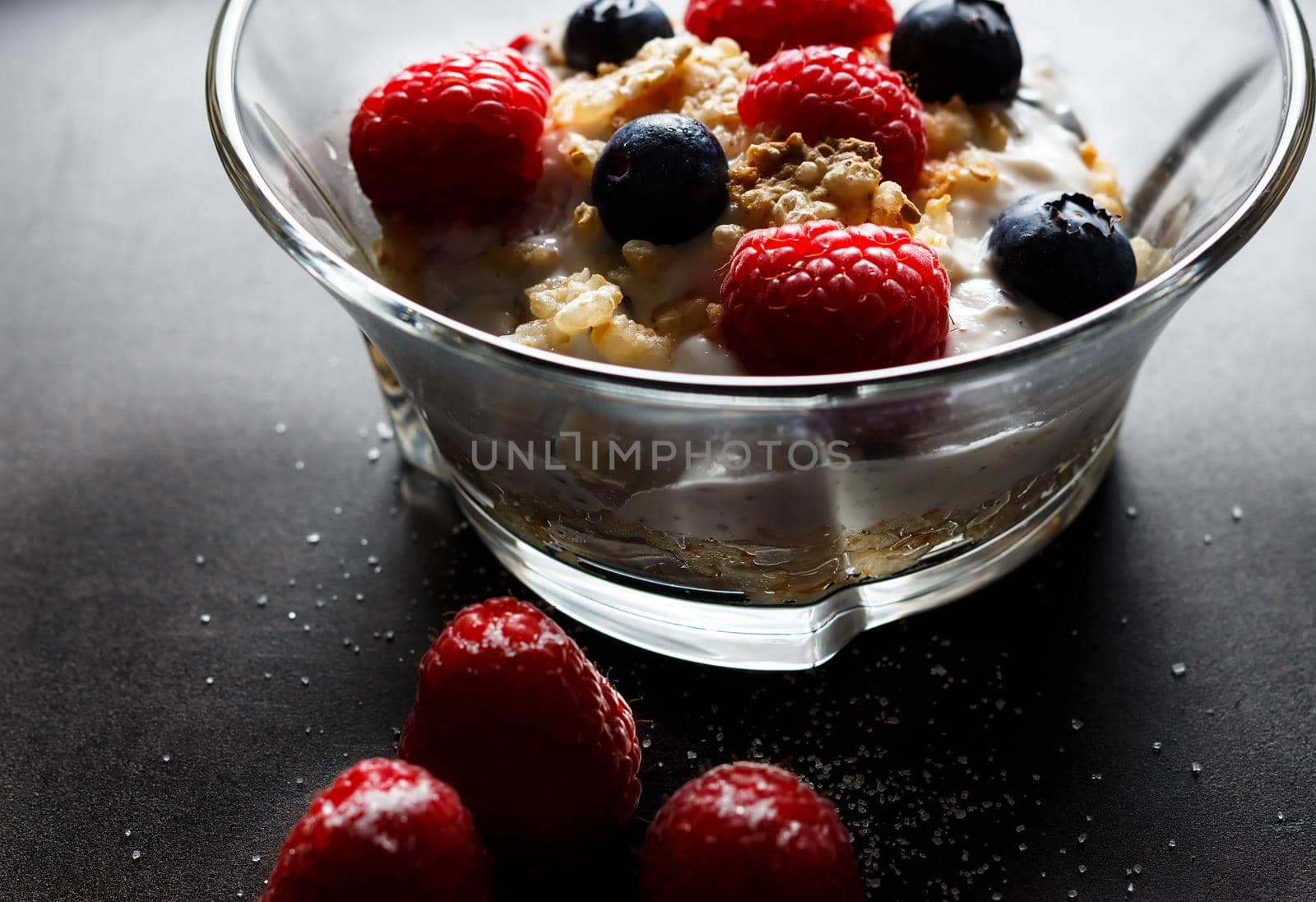 Raspberries, blueberries, cereals and yogurt in a glass bowl on a black surface. Healthy breakfast for a healthy life. Horizontal image.