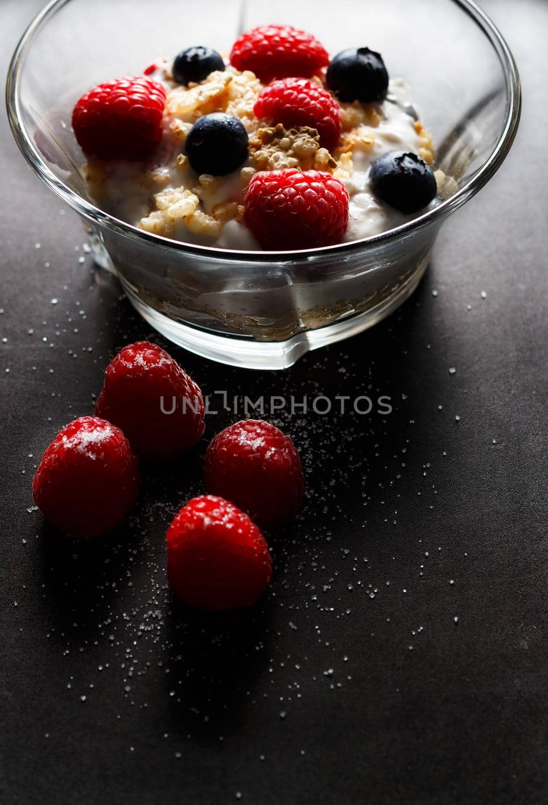 Raspberries, blueberries, cereals and yogurt in a glass bowl on a black surface. Healthy breakfast for a healthy life. Vertical image.